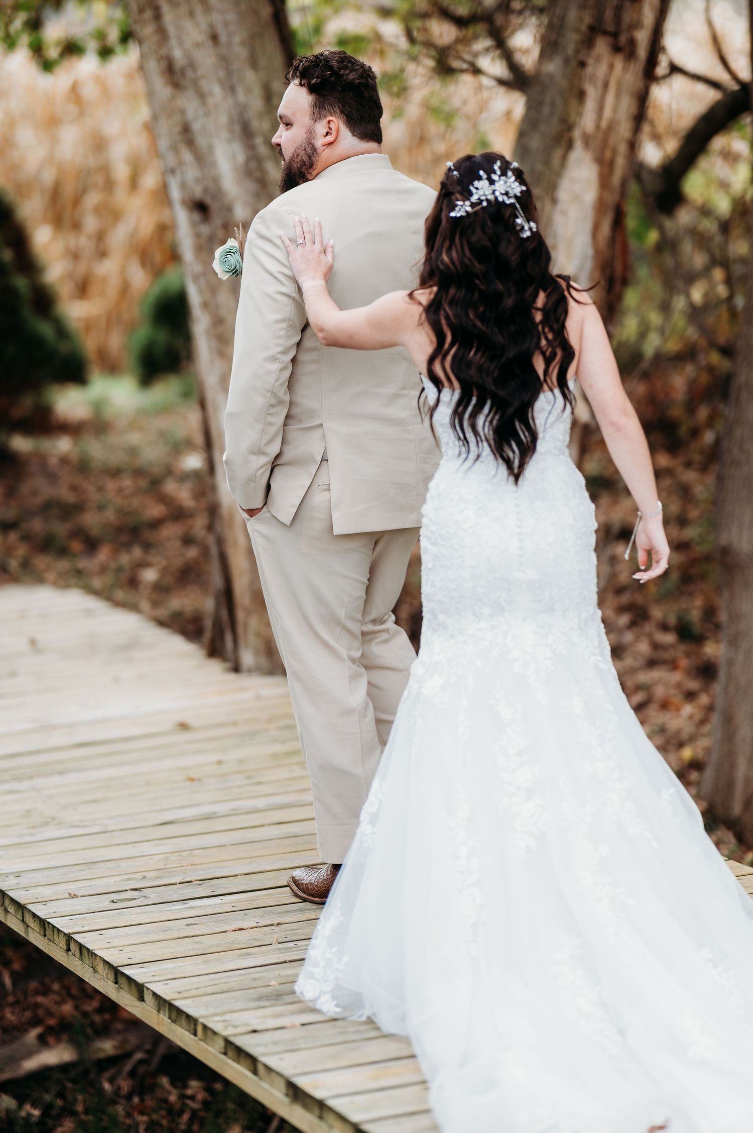 A couple in wedding attire share a romantic moment on a wooden boardwalk in an outdoor setting.