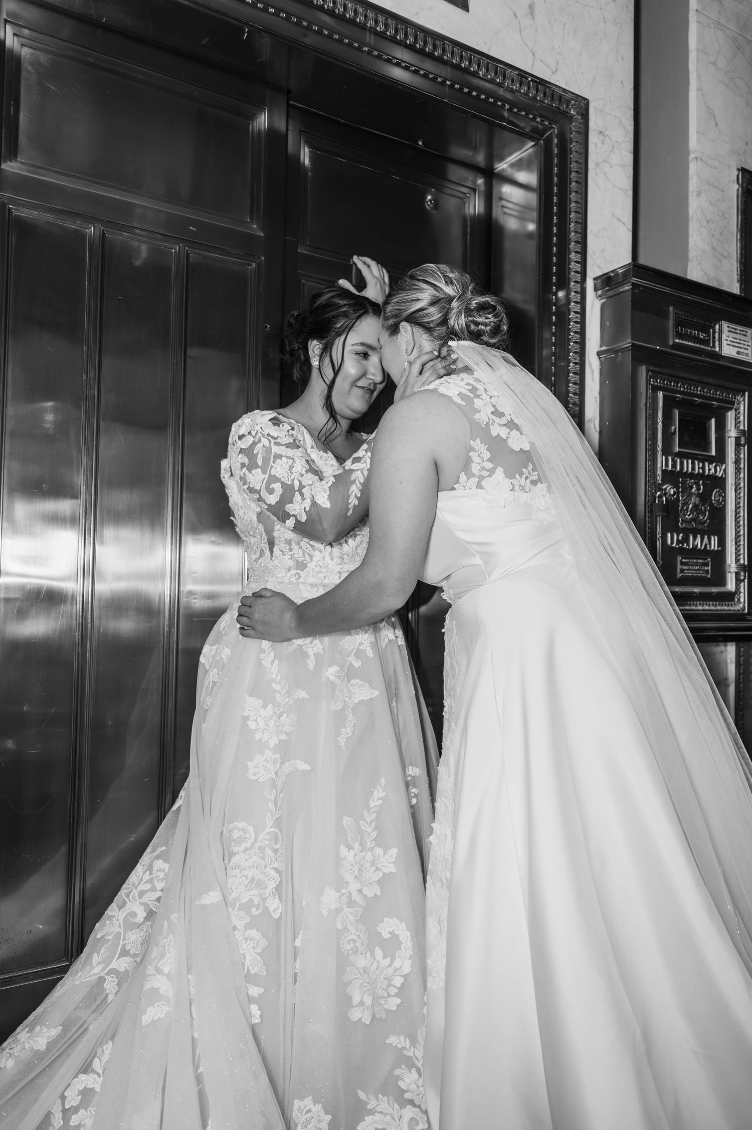 Two people in wedding attire share an intimate moment in an elegant hallway.