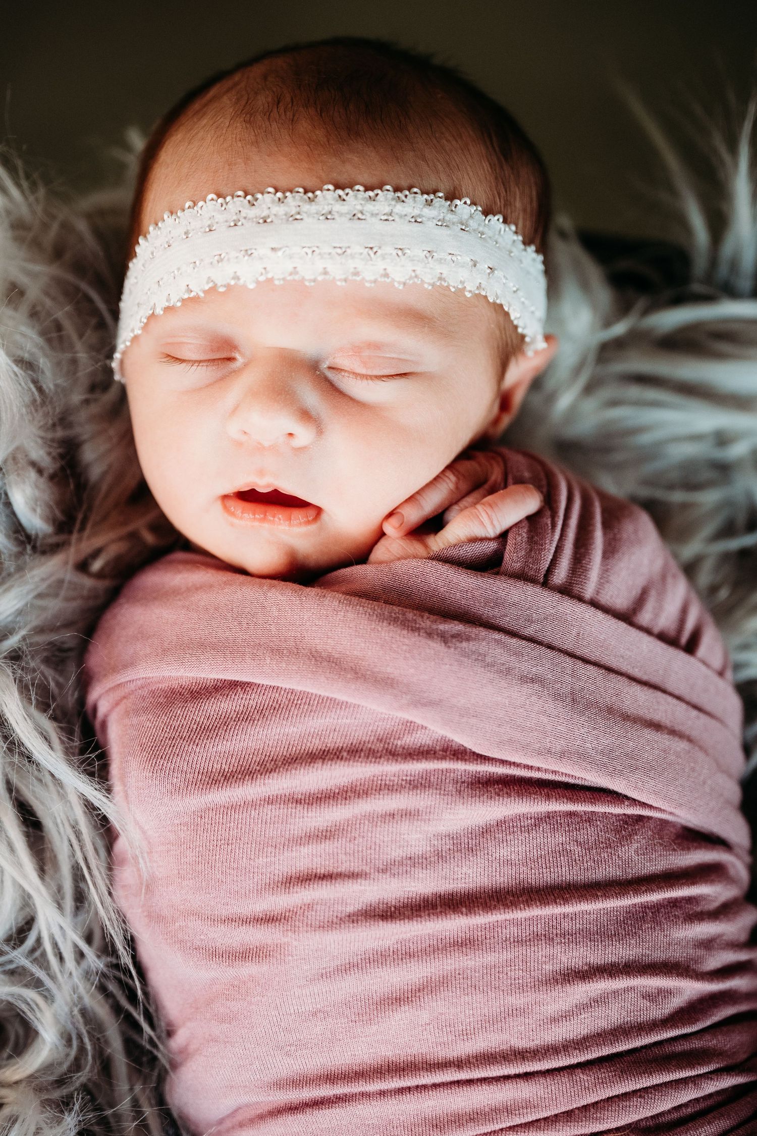 Newborn baby sleeping peacefully wrapped in soft pink blanket with delicate white lace details.