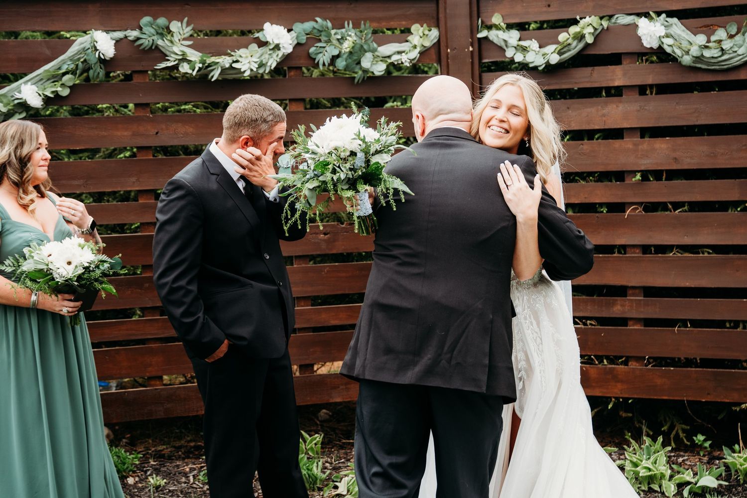 A couple shares an intimate dance moment during their wedding celebration with floral decor and wooden backdrop.