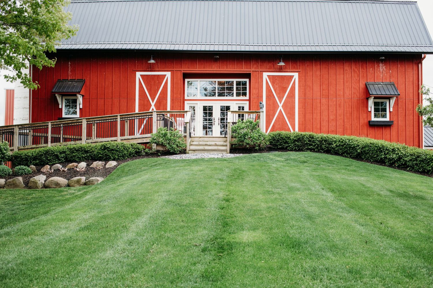 A bright red barn with white trim and a well-manicured green lawn features classic double doors and landscaping.