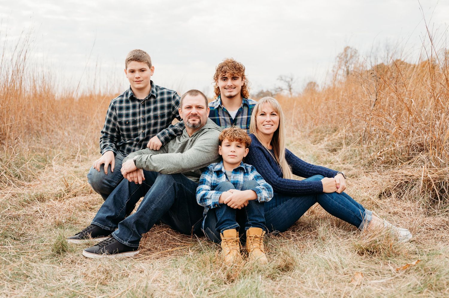 A family of five poses together while sitting in a fall field with tall golden grass.