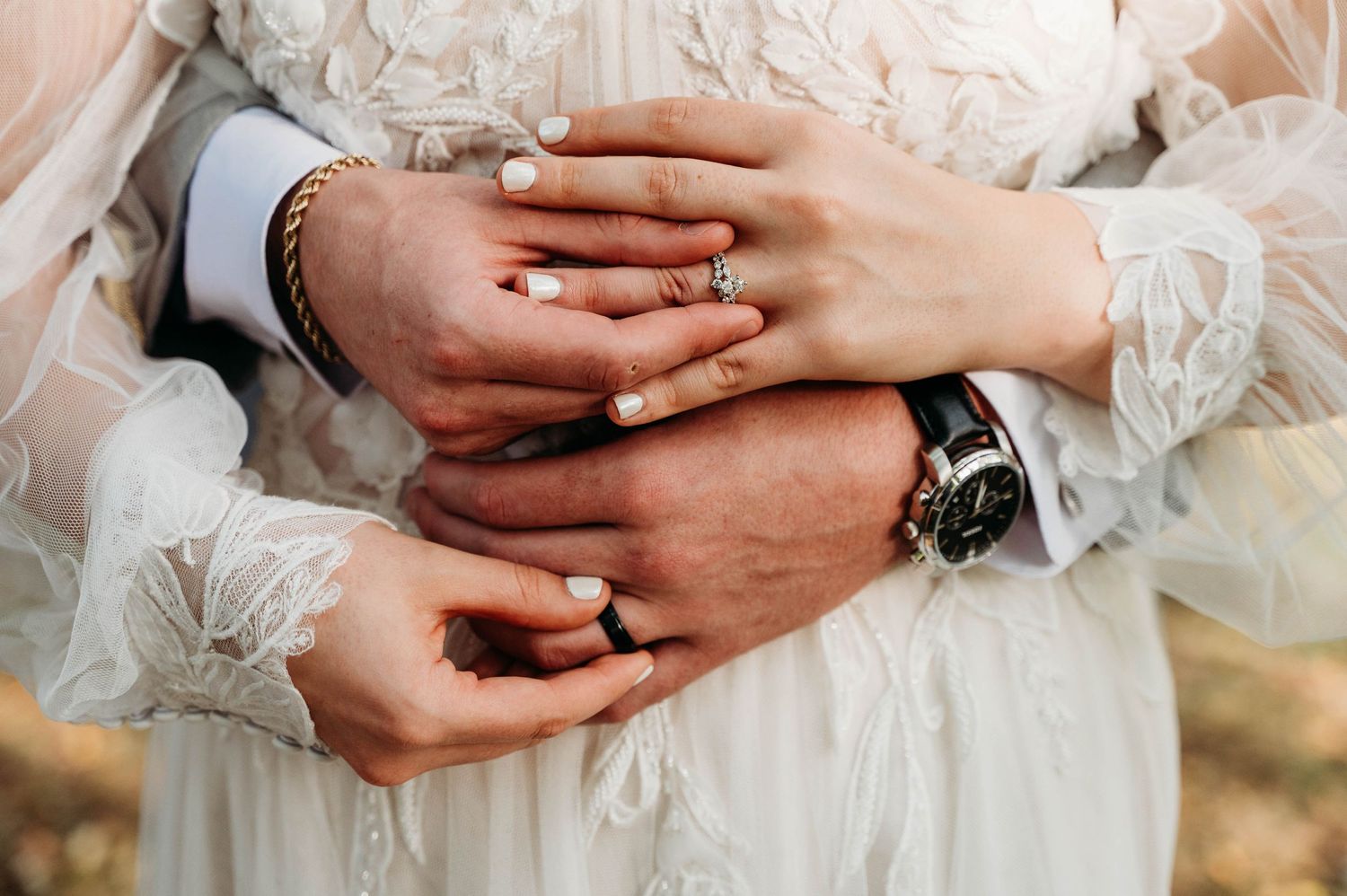 Close-up shot of hands displaying wedding rings against delicate white lace dress fabric.