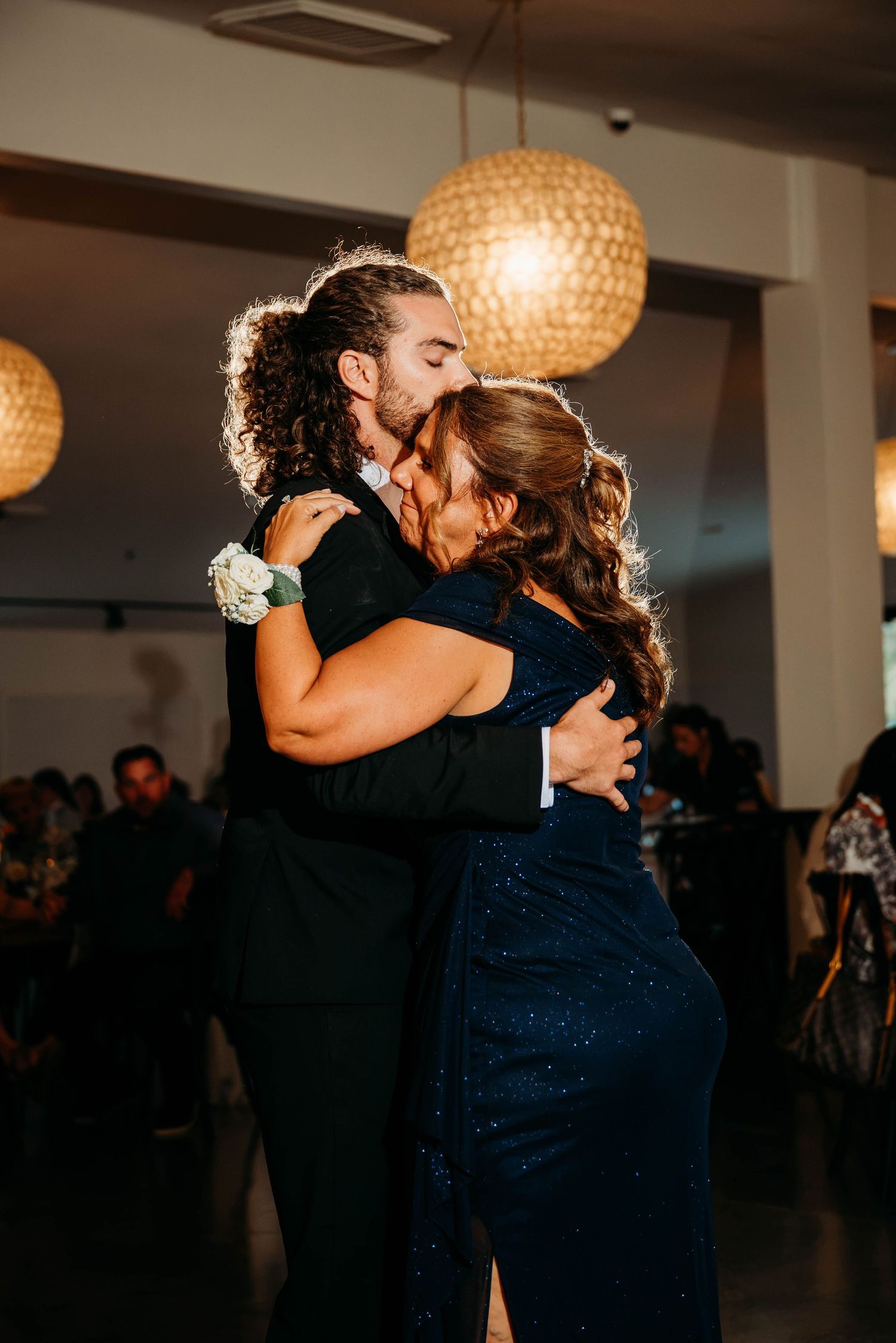 Couple sharing a romantic dance and embrace at a formal wedding reception under warm globe pendant lights.