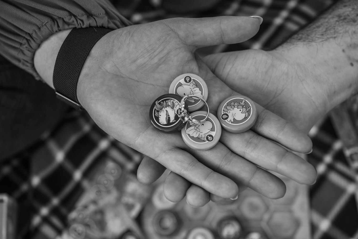 Black and white photo of a hand holding several small round coins or tokens with decorative designs.