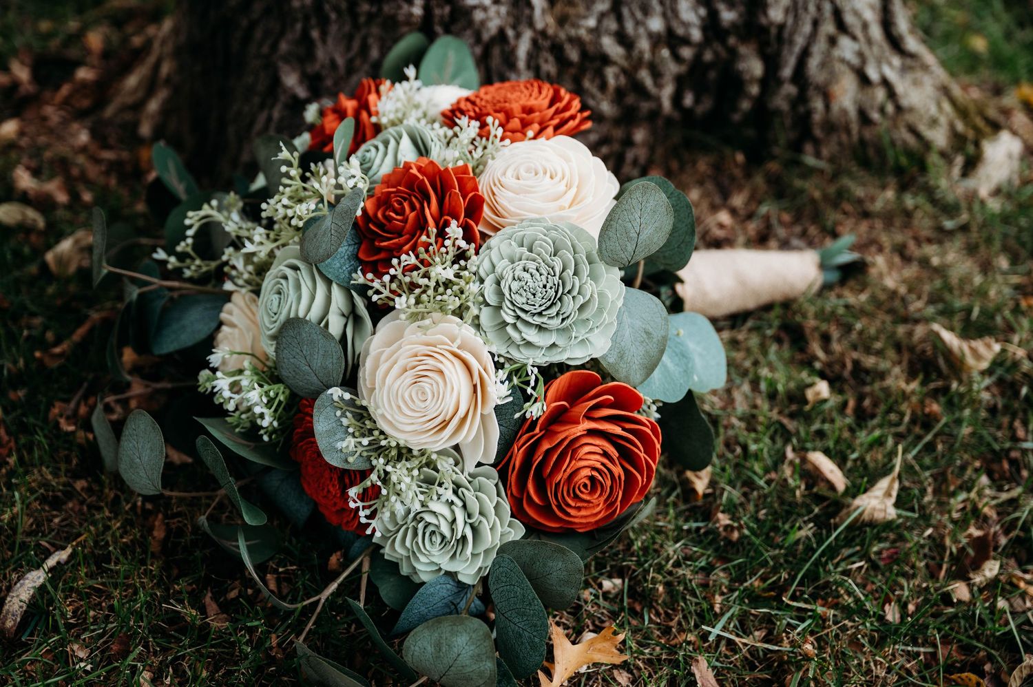 An elegant bridal bouquet with red and white flowers mixed with eucalyptus leaves rests on grass.