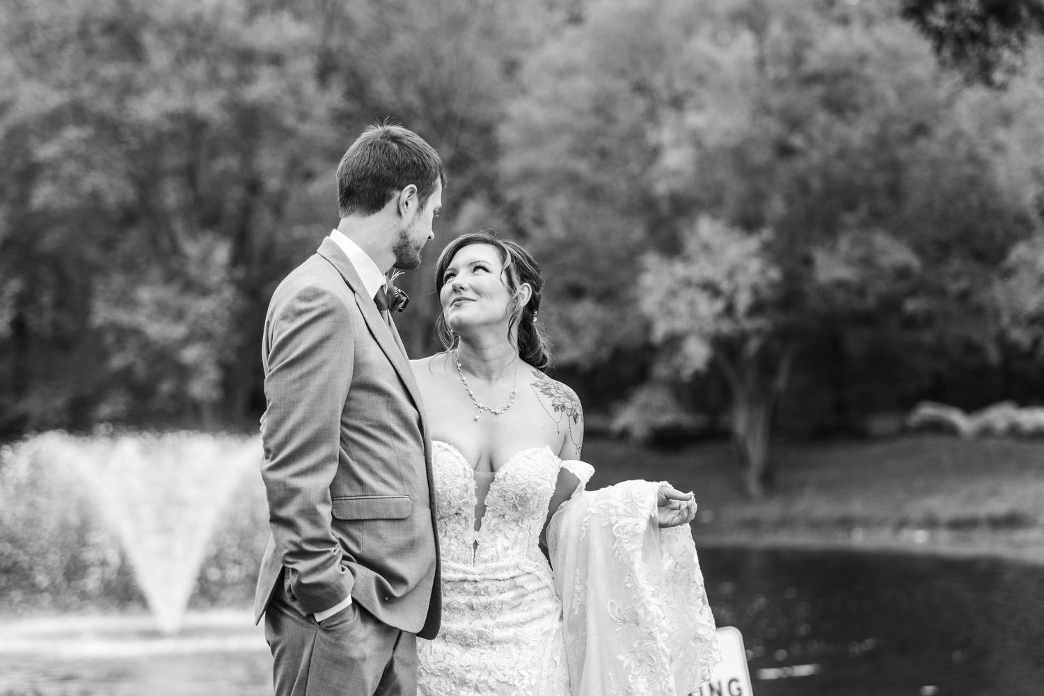 Black and white photo of a bride and groom sharing a romantic moment near a fountain outdoors.