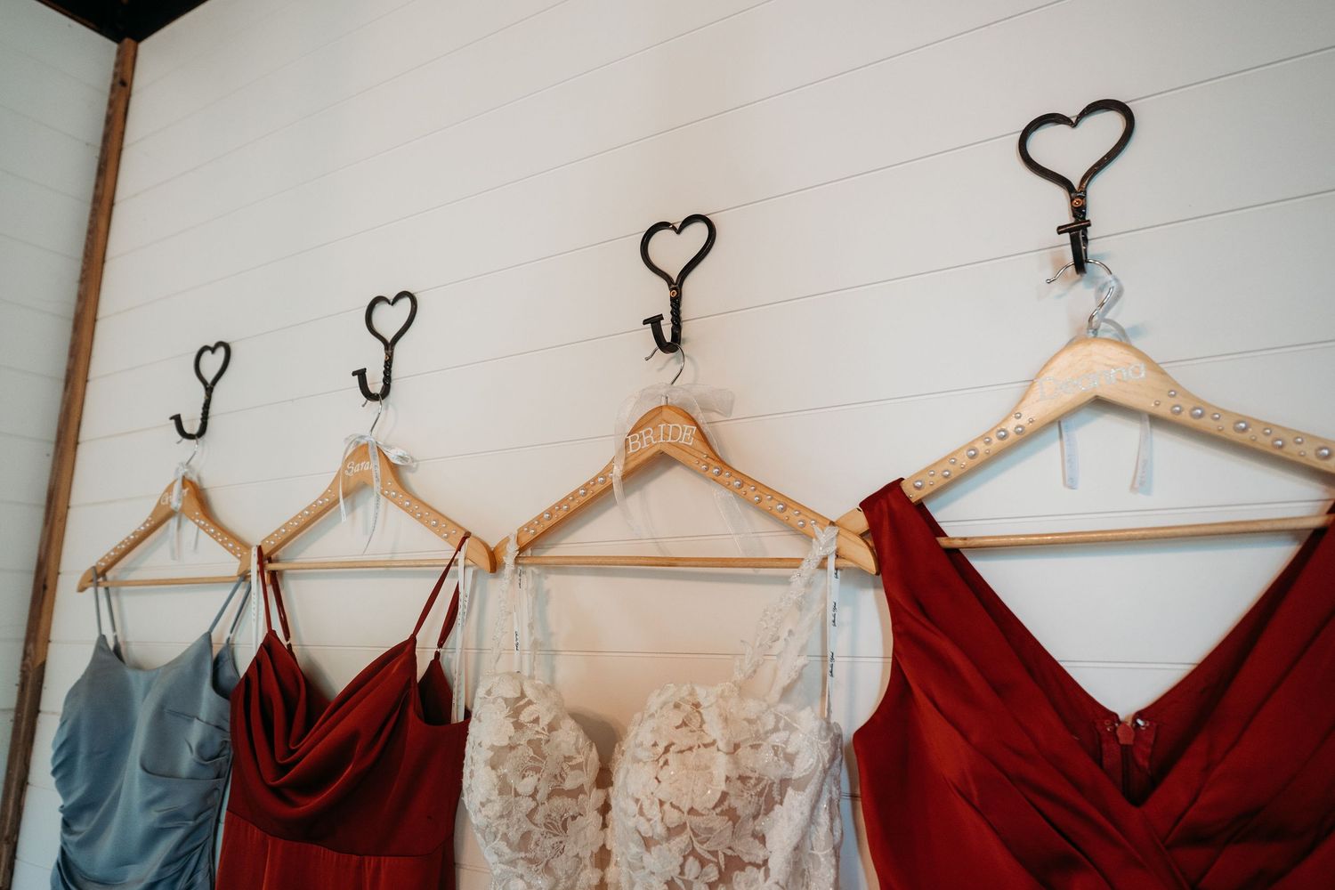 Wedding dresses and bridesmaid gowns in burgundy and blue hang from heart-shaped wall hooks.