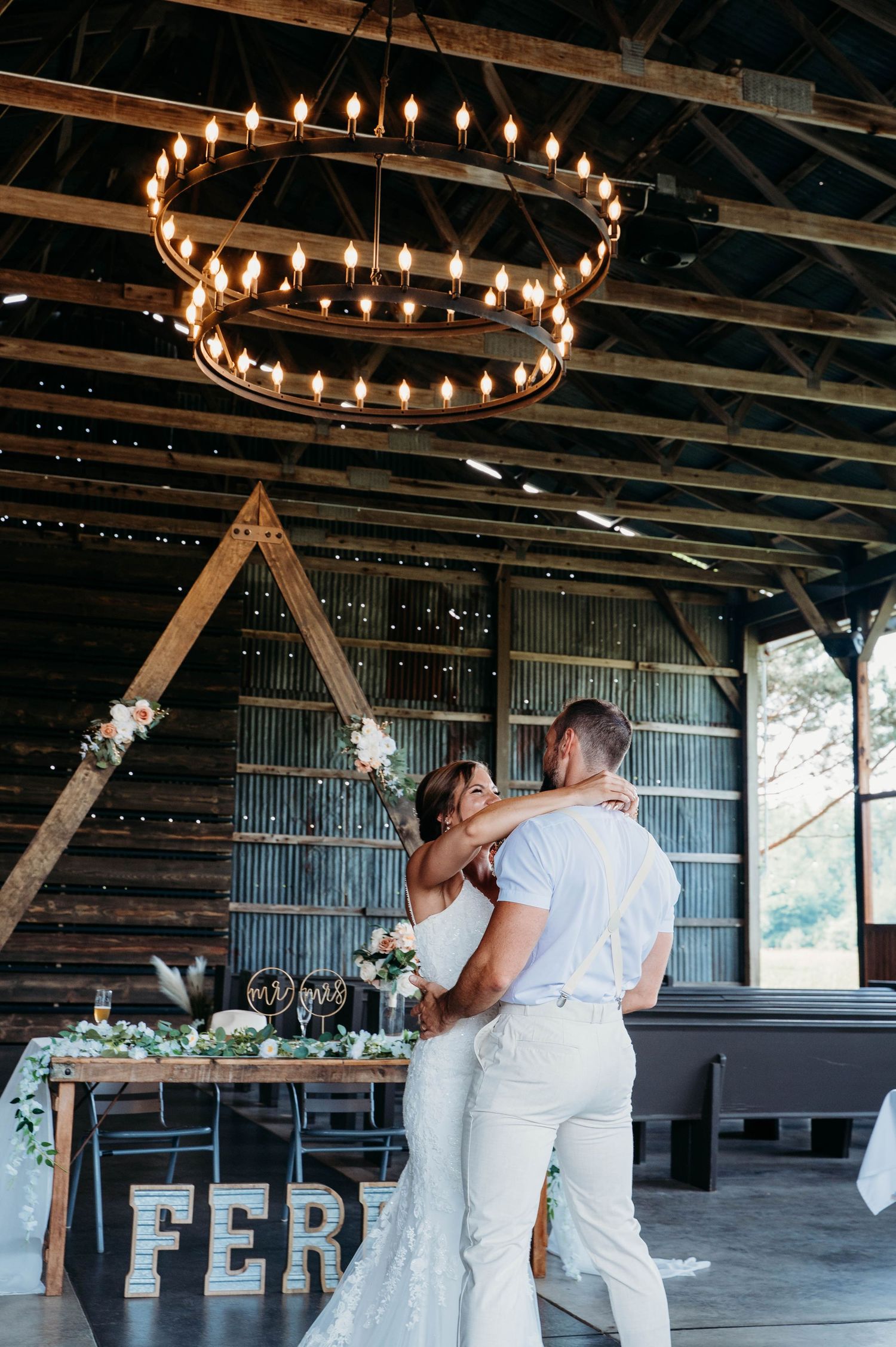 Rustic barn venue with circular chandeliers and string lights decorated for wedding reception.