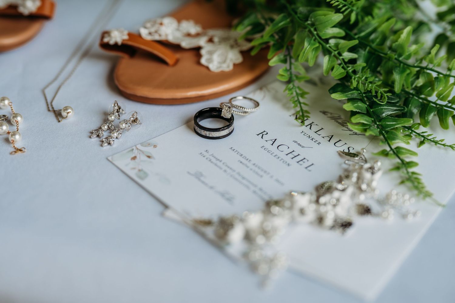 Wedding details with rings, delicate white flowers, and greenery arranged on a rustic wooden surface.