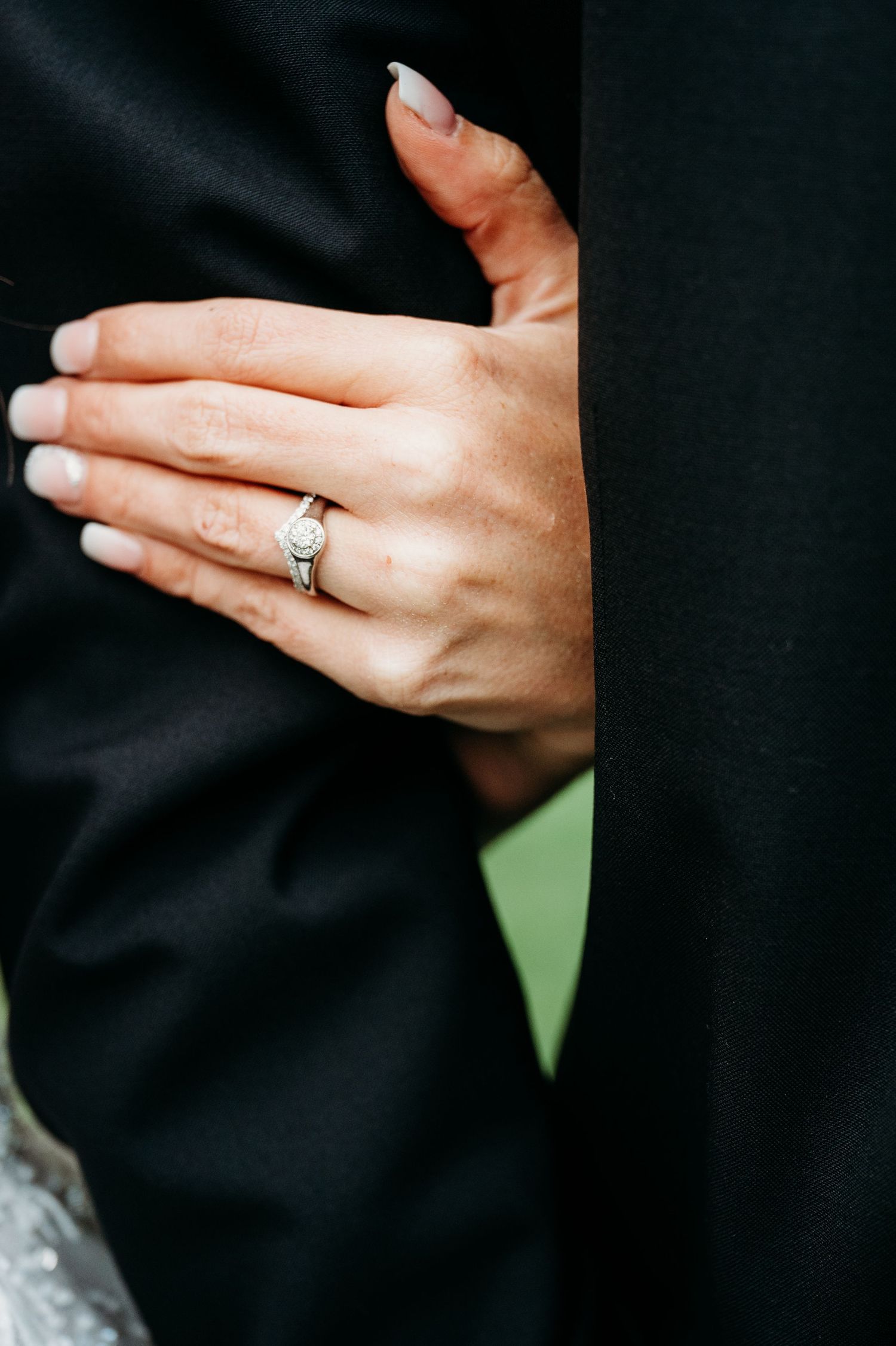 Close-up of an elegant diamond engagement ring on a hand against a black background.