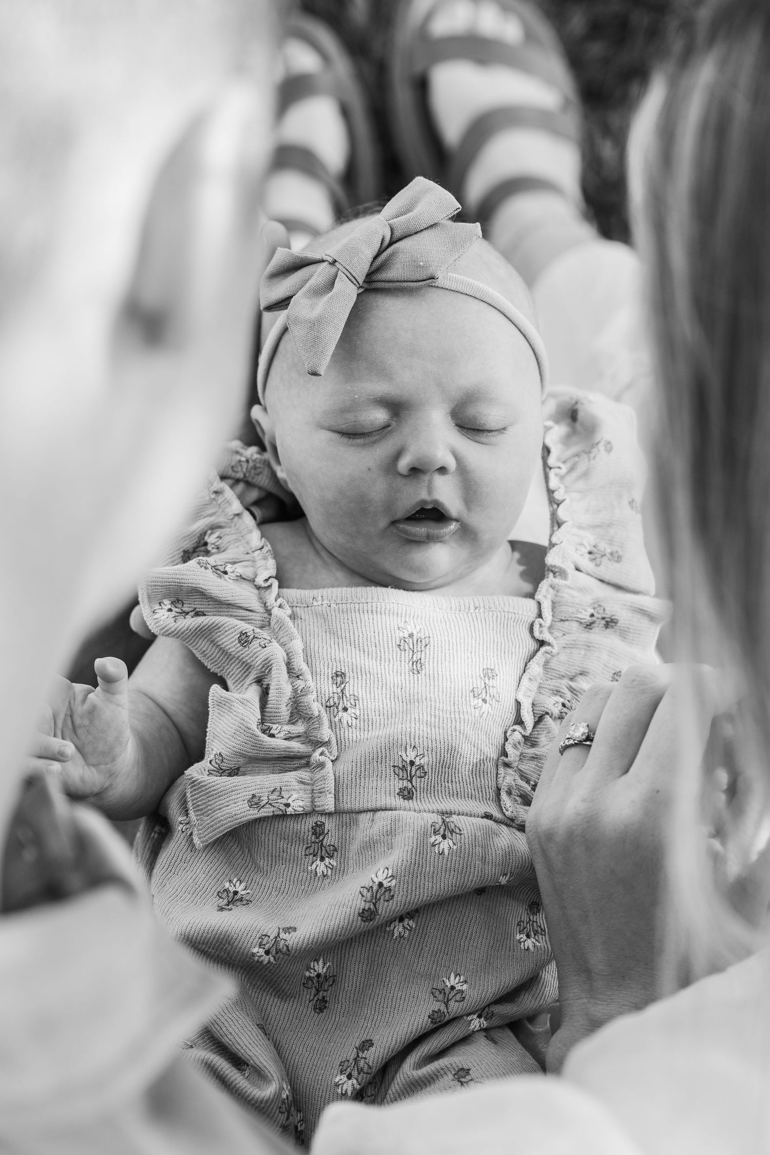 A sleeping baby wearing a floral romper and bow headband in a black and white photograph.