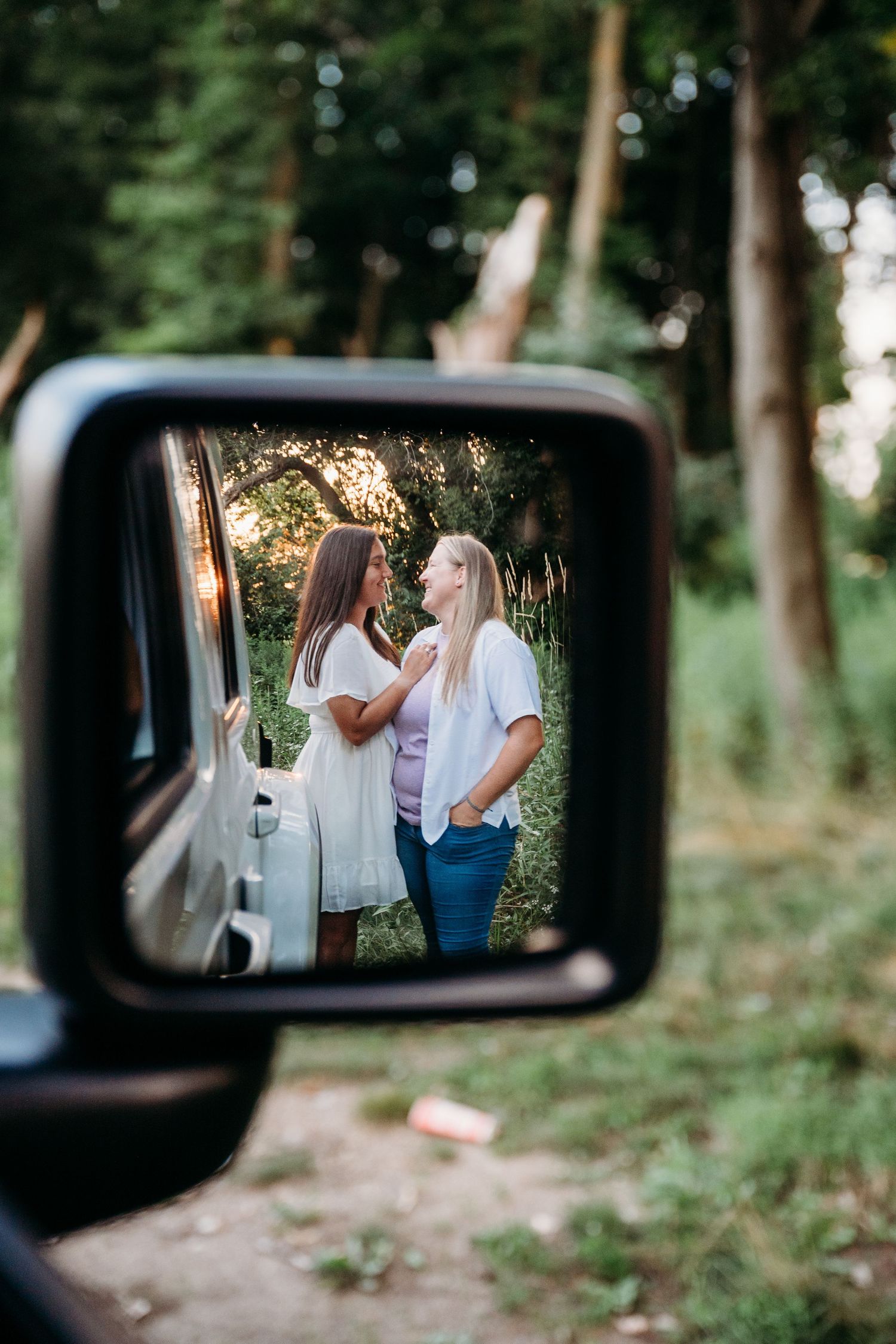 A creative engagement photo series reflected in a car side mirror showing a couple in a wooded setting.