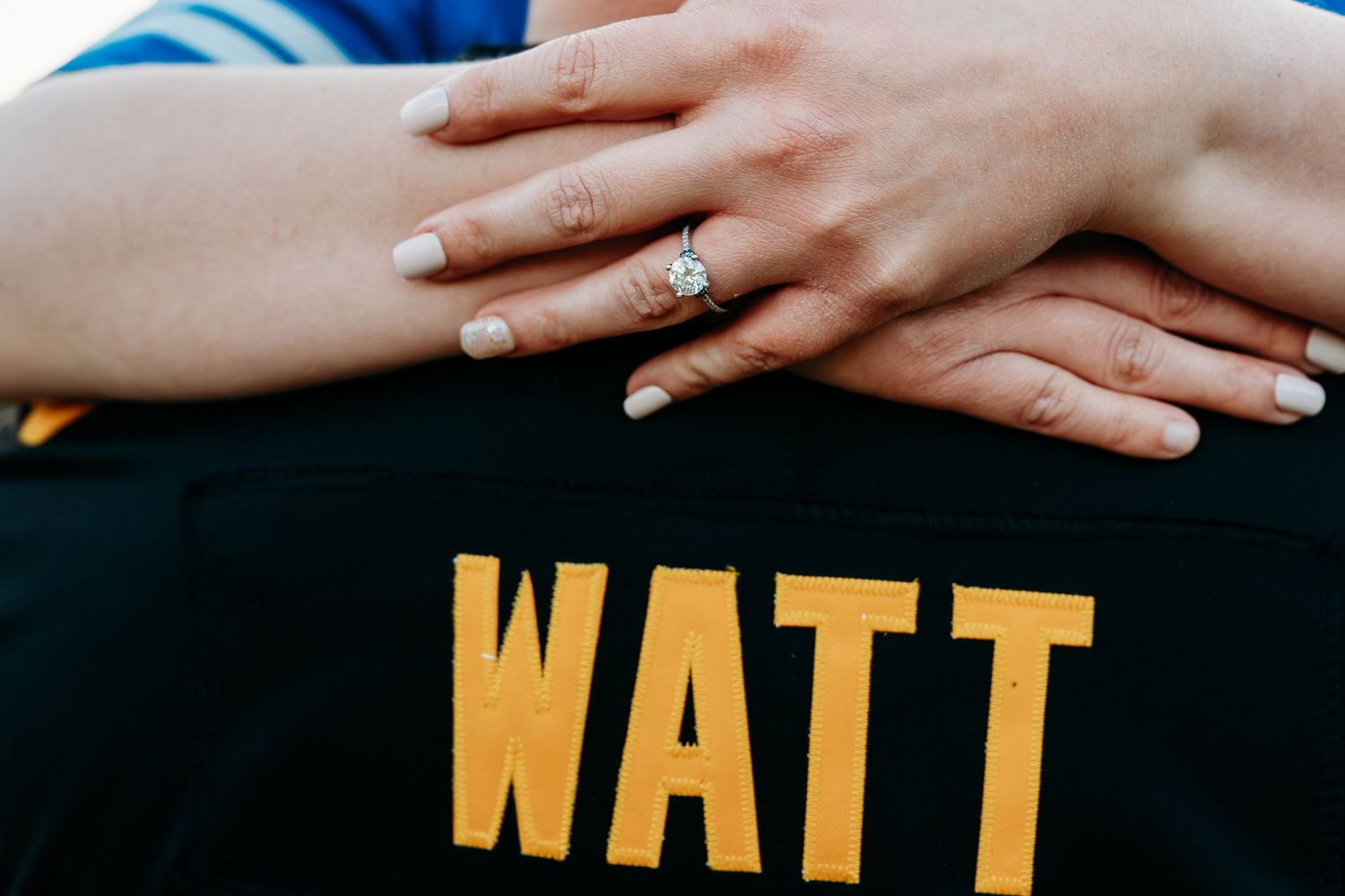 Close-up of an engagement ring on a woman's hand resting on a WATT jersey.