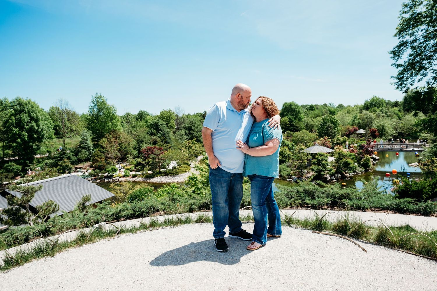 Older couple sharing a romantic kiss outdoors at a scenic garden overlook on a sunny day.