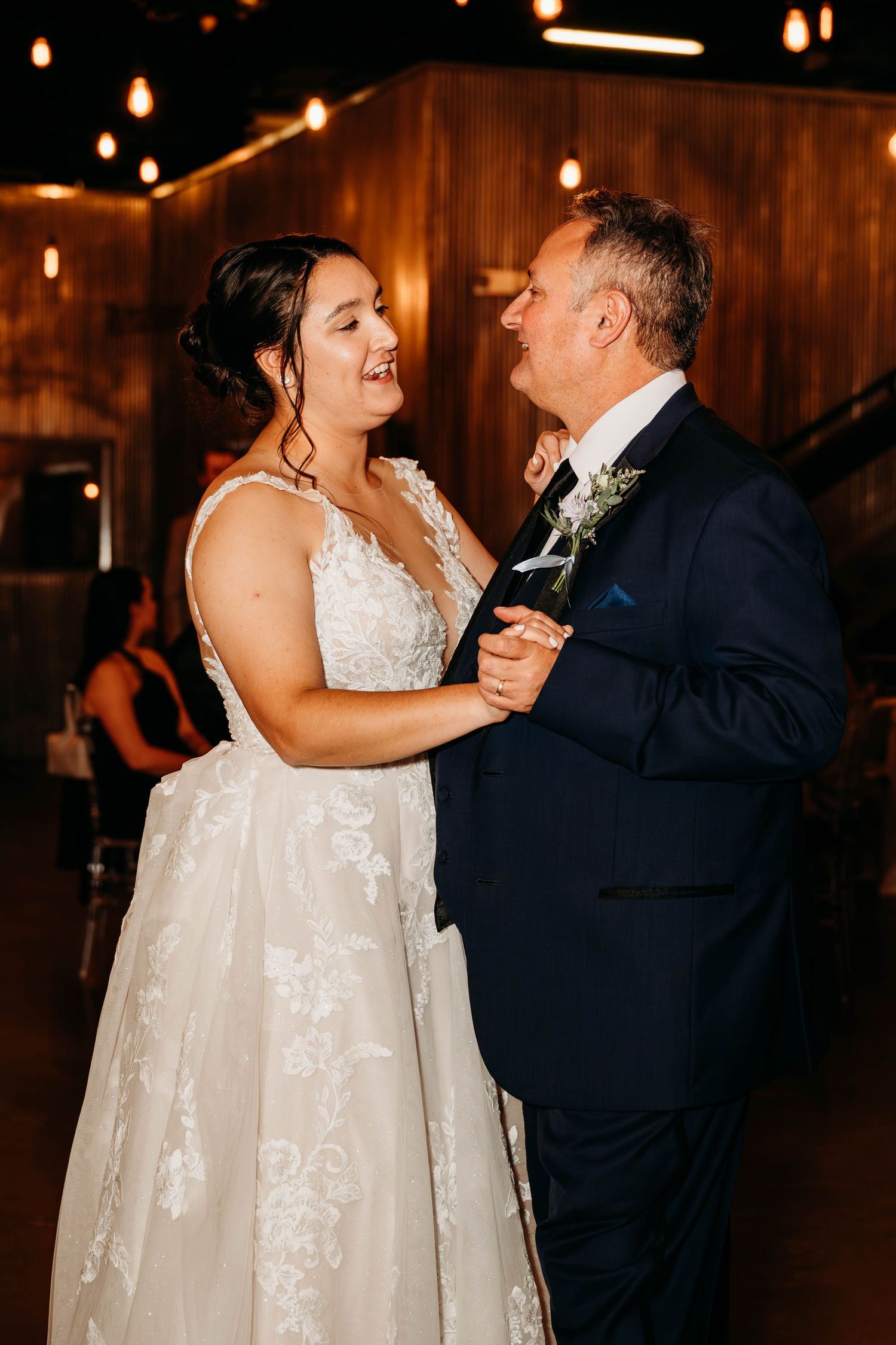 Wedding couple dancing together in formal attire under warm reception lighting.