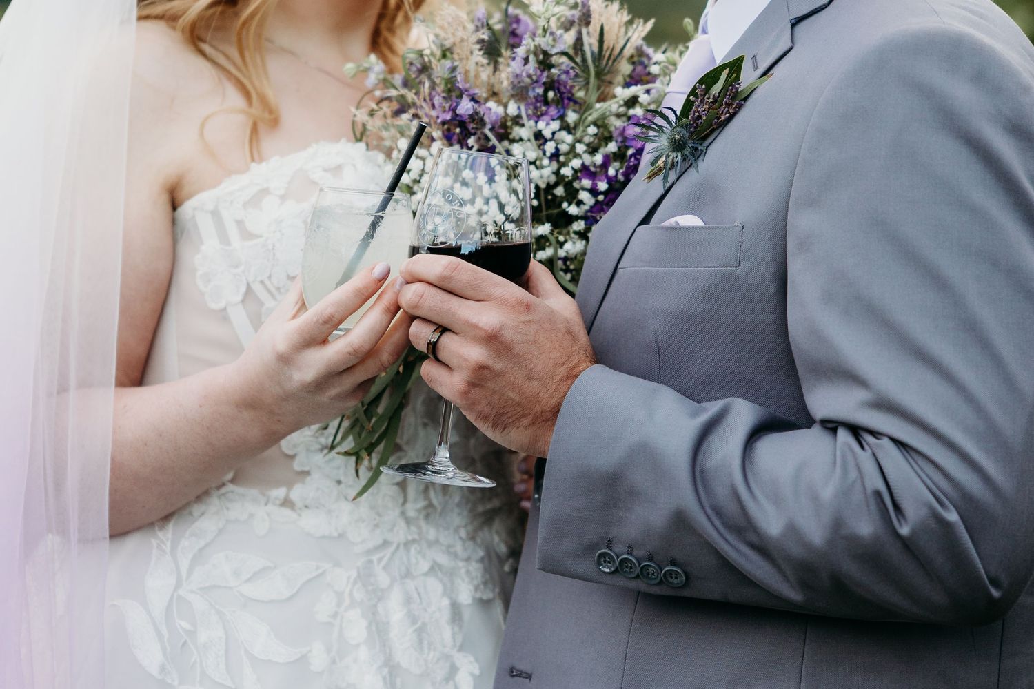 A bride and groom exchange rings during an outdoor wedding ceremony surrounded by floral arrangements.