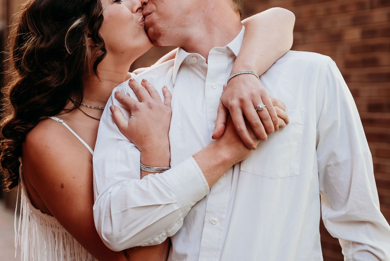 A tender romantic embrace between a couple dressed in white as they share an intimate kiss against a brick wall.