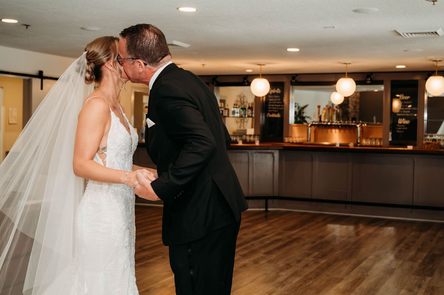 Bride and groom share their first dance kiss in an elegant wedding reception venue with warm lighting.