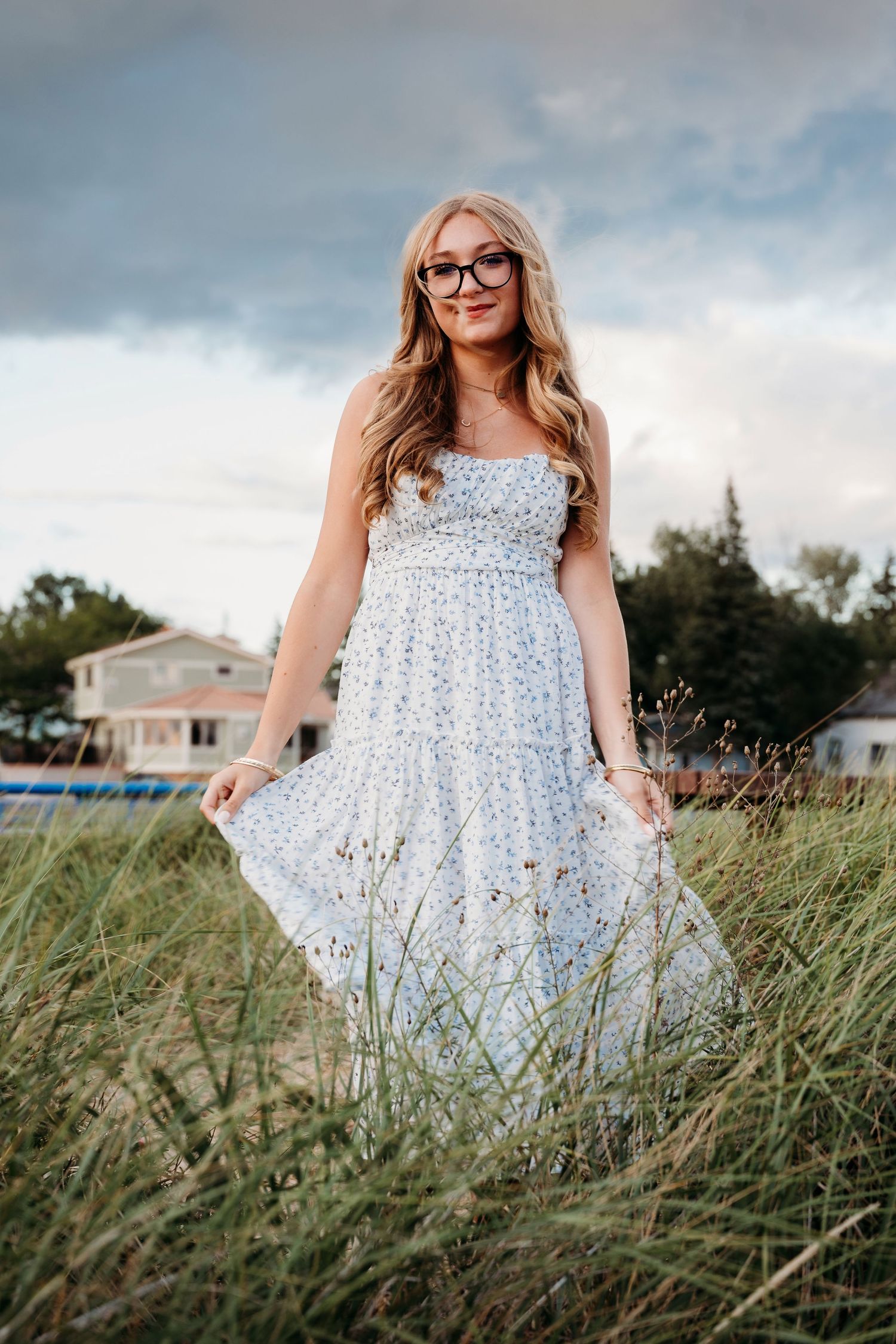 A field photoshoot featuring a summery white floral dress against tall grasses and cloudy skies.