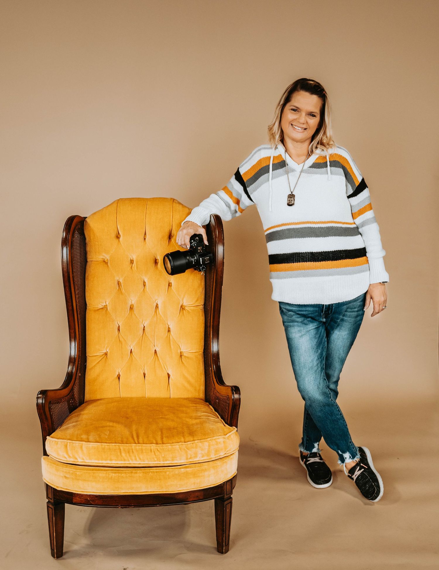 Casual portrait next to a vintage yellow tufted chair wearing a striped sweater and jeans.