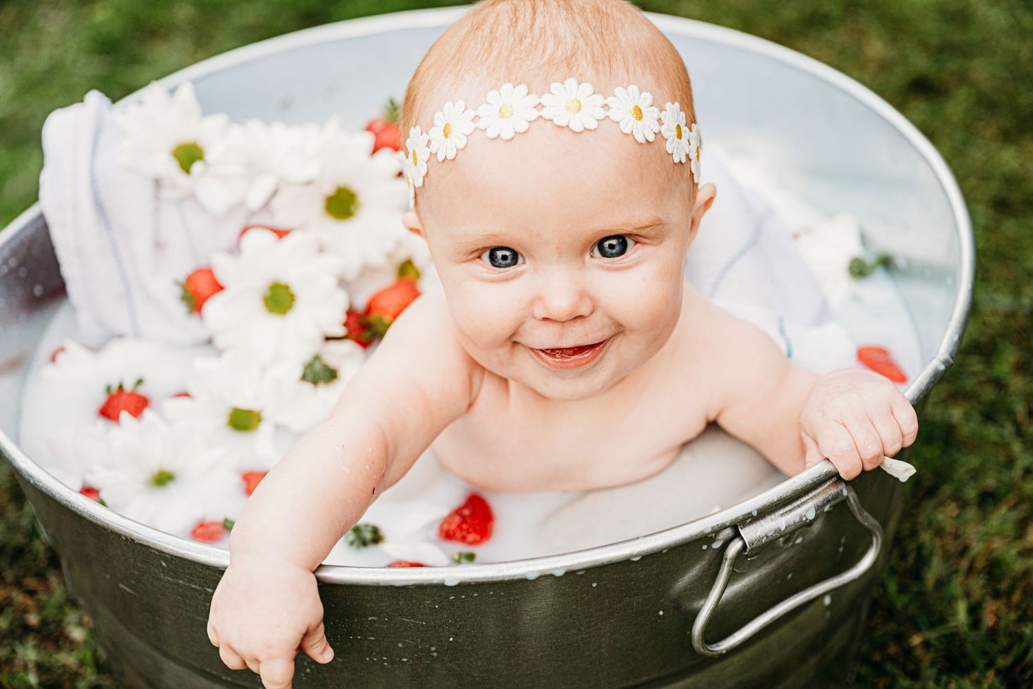 A baby bath photography session with flowers and milk in a vintage metal tub outdoors.