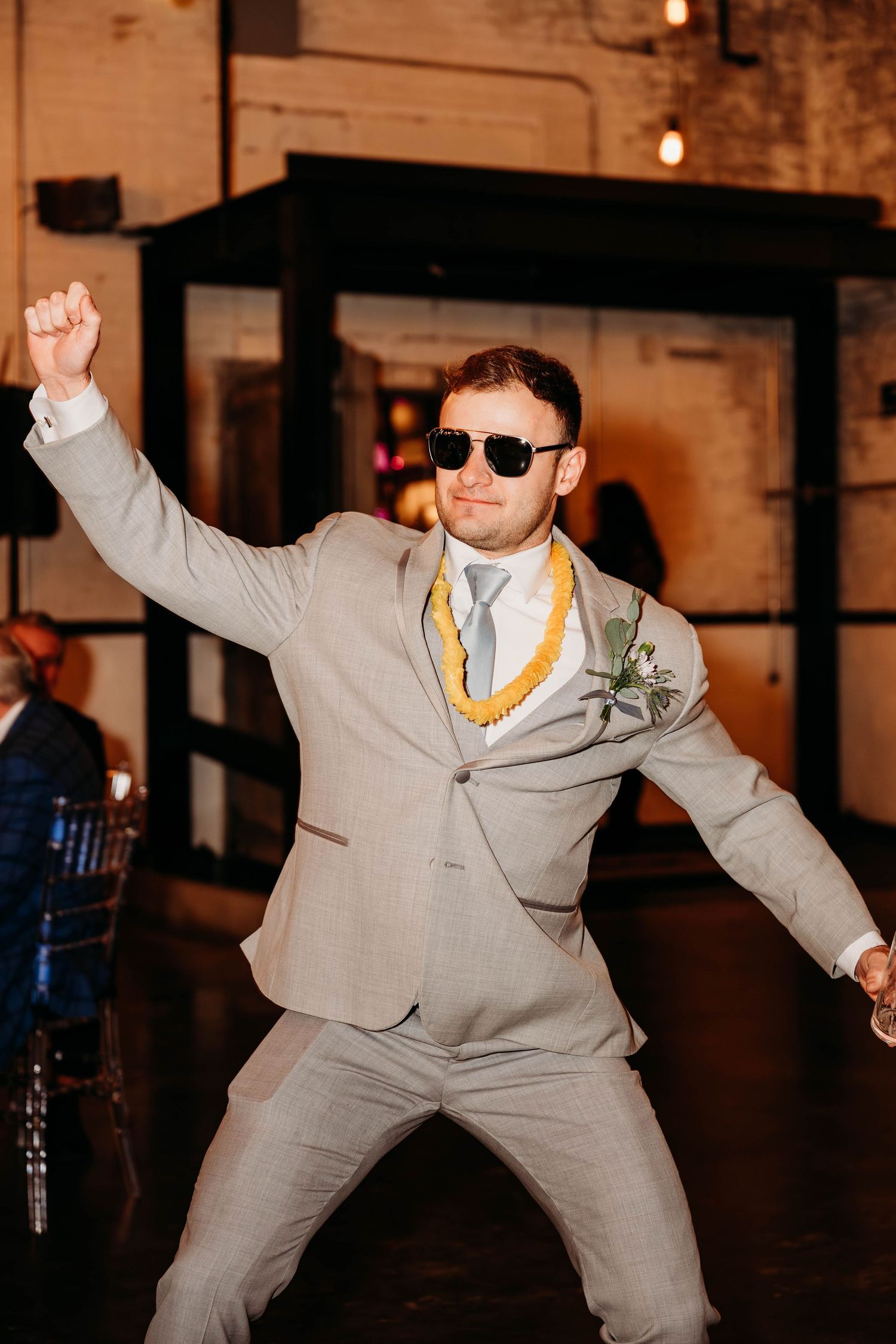 Wedding guest in grey suit and sunglasses dancing enthusiastically at reception.