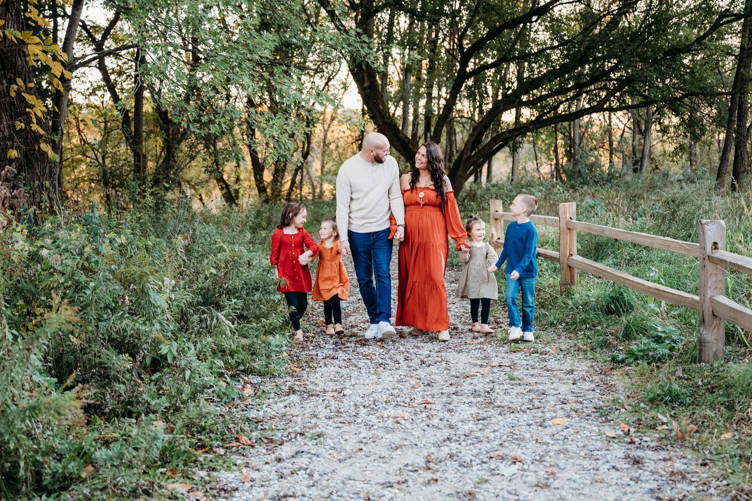 A family walks together on a gravel path through a wooded area on an autumn afternoon.