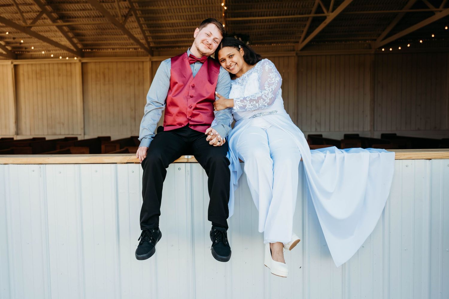 Two people sit together on a white barn wall, their feet dangling over the edge.