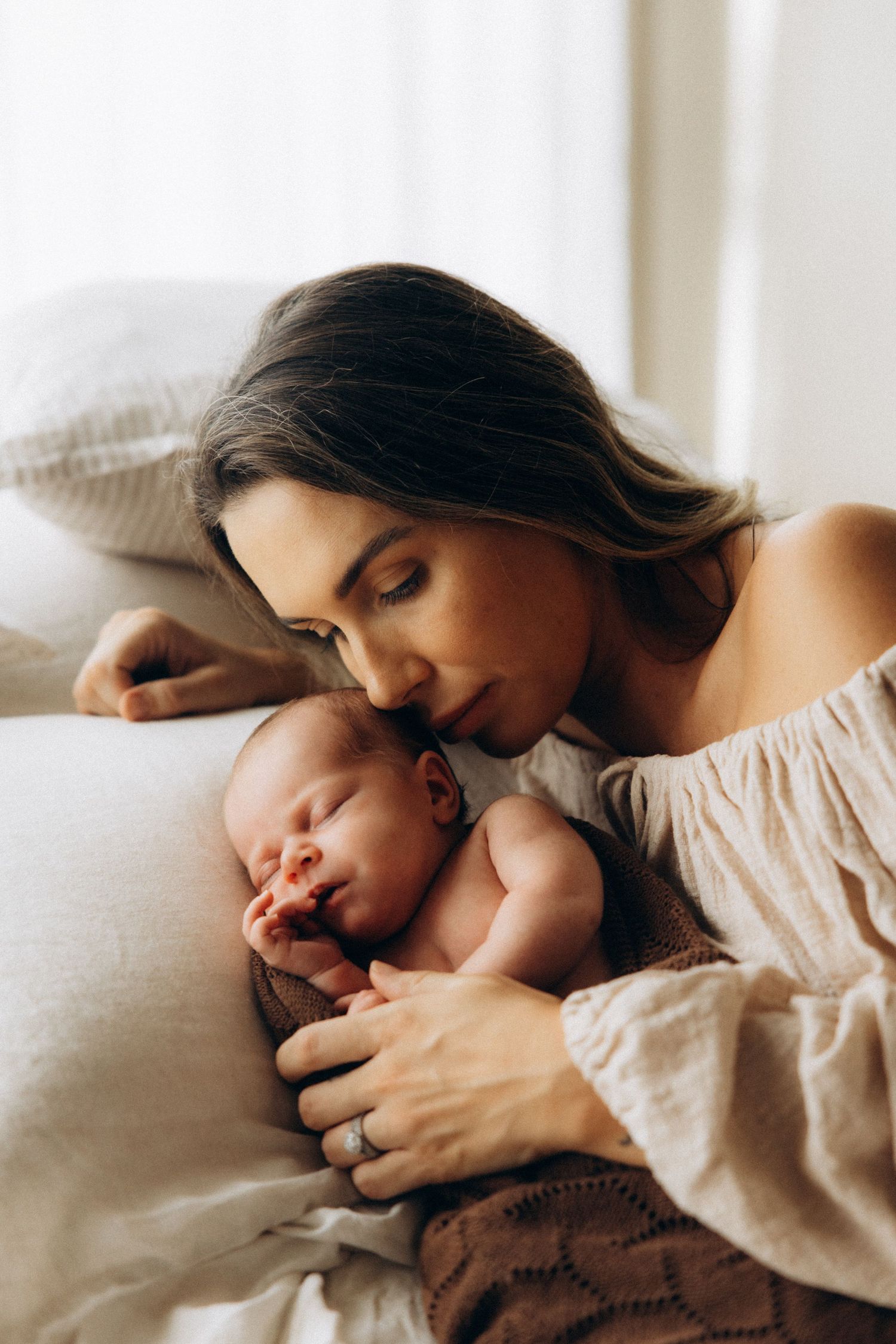 Mother and sleeping newborn share peaceful moment on white bedding.
