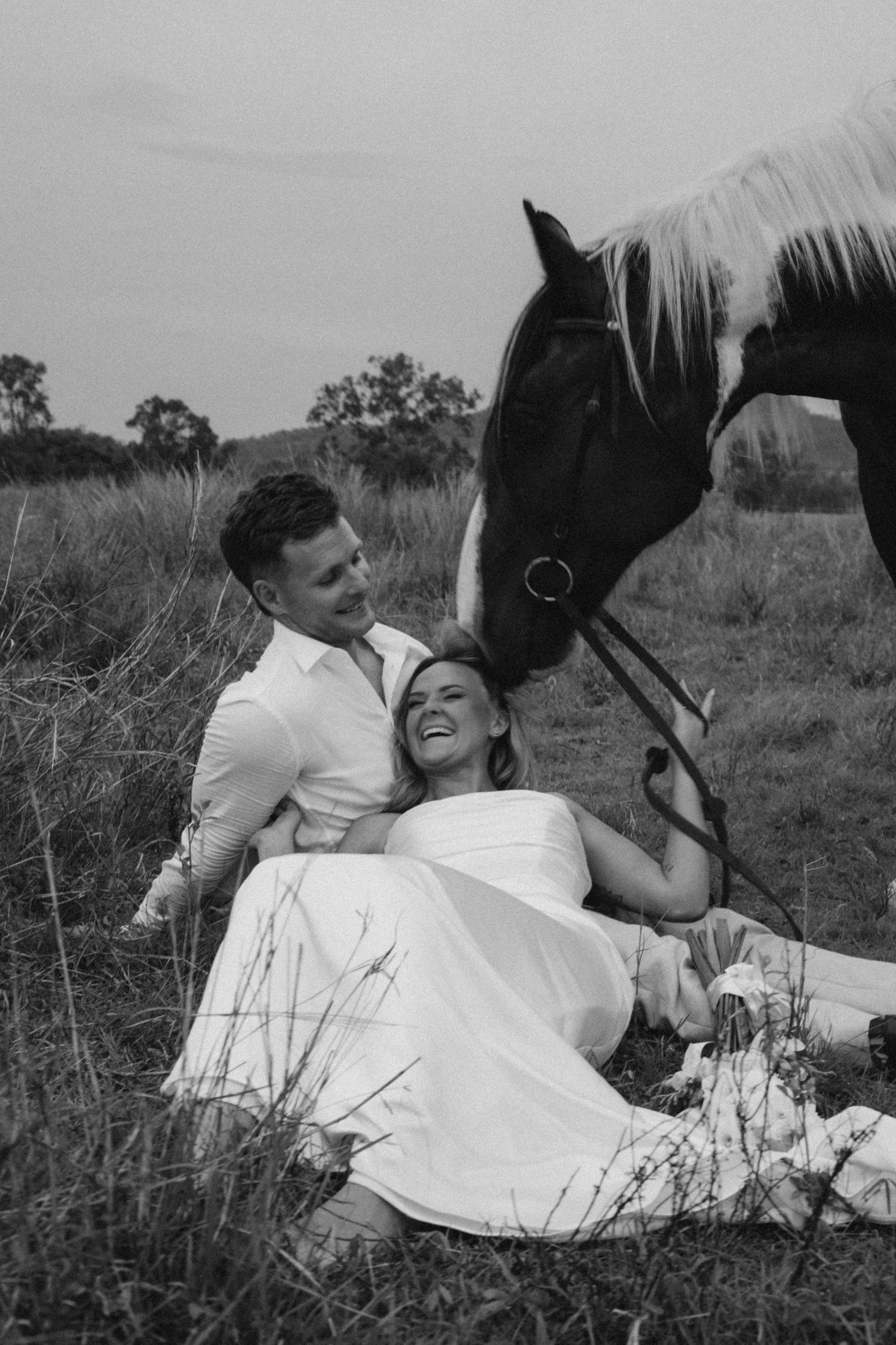Black and white wedding photos showing tender moments with a horse in tall grass.