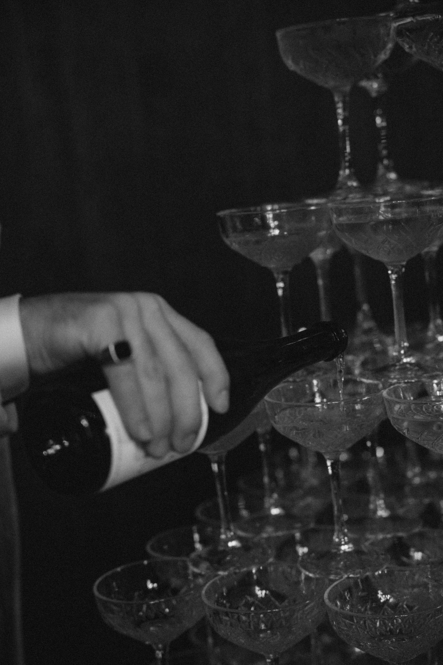 Hands carefully pouring champagne into a tower of crystal glasses at a reception.