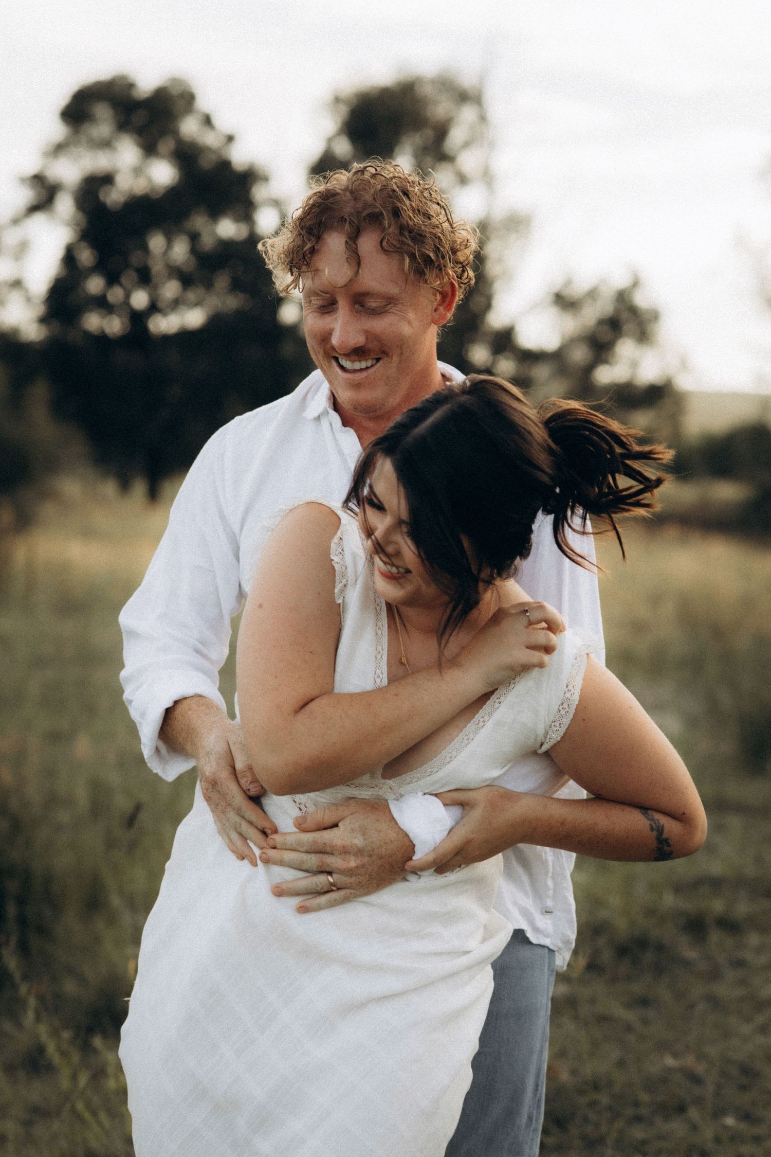 Playful couple embracing and laughing together in an outdoor field.