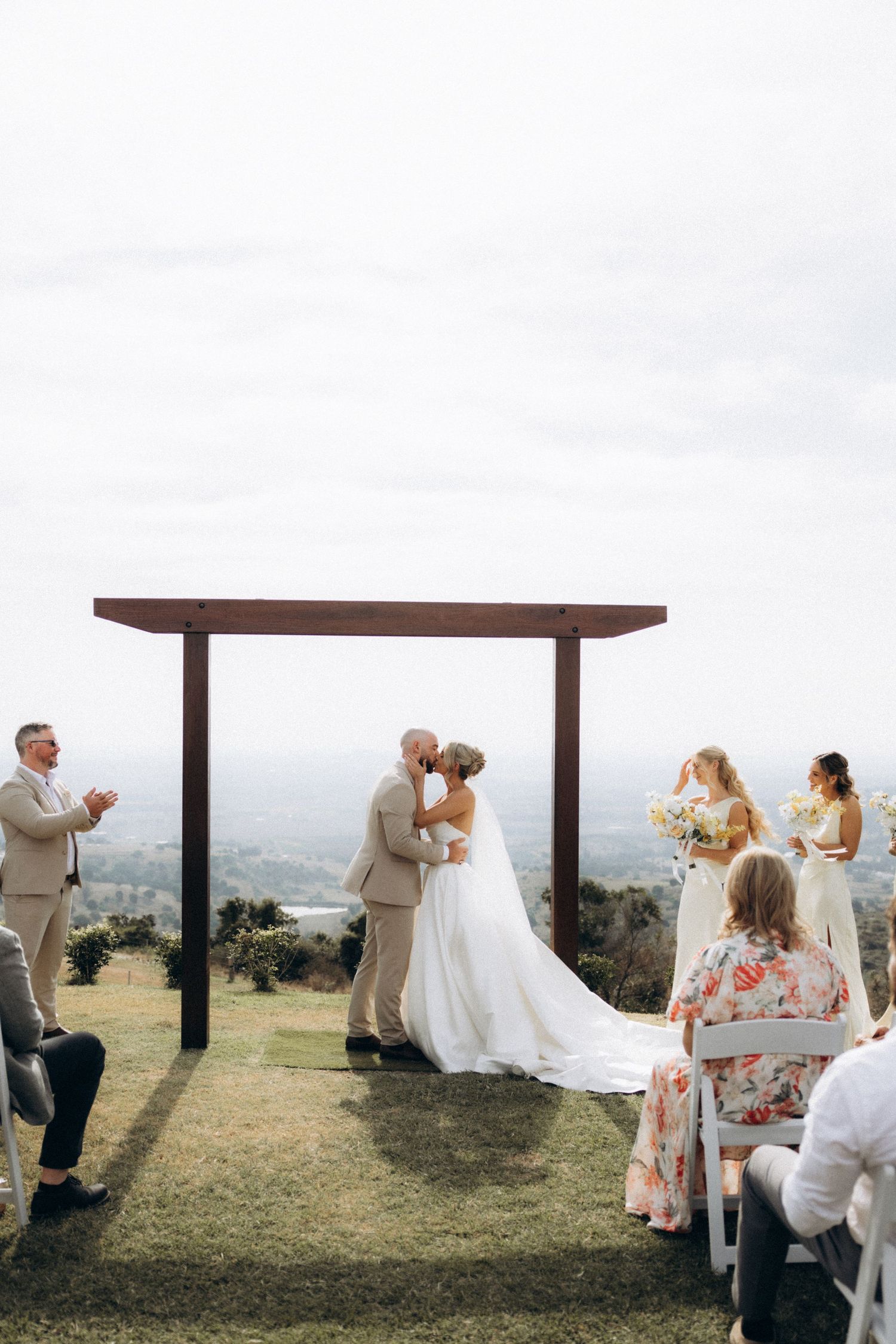 Outdoor wedding ceremony under wooden pergola with scenic mountain backdrop.