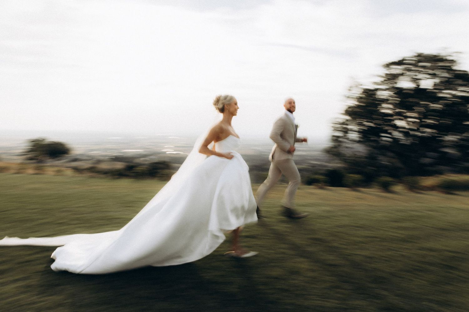 Artistic sequence of newlyweds walking across a hilltop with dress flowing in the wind.