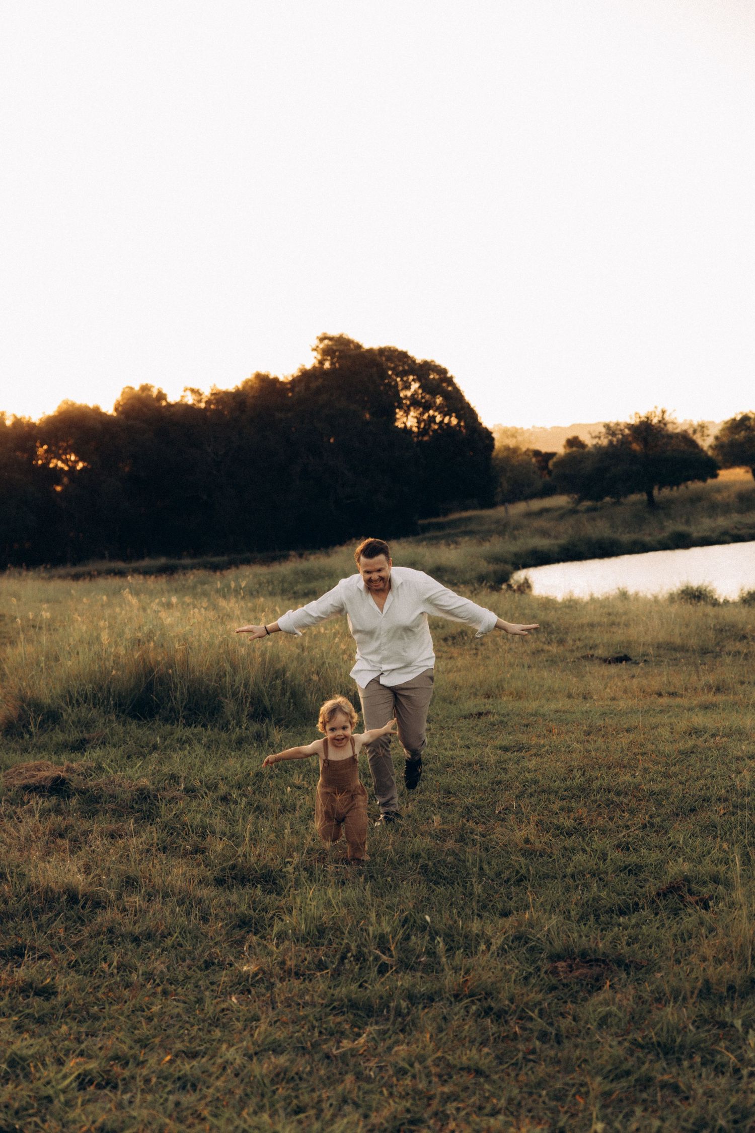 A playful moment captured at sunset in a grassy field near a lake.