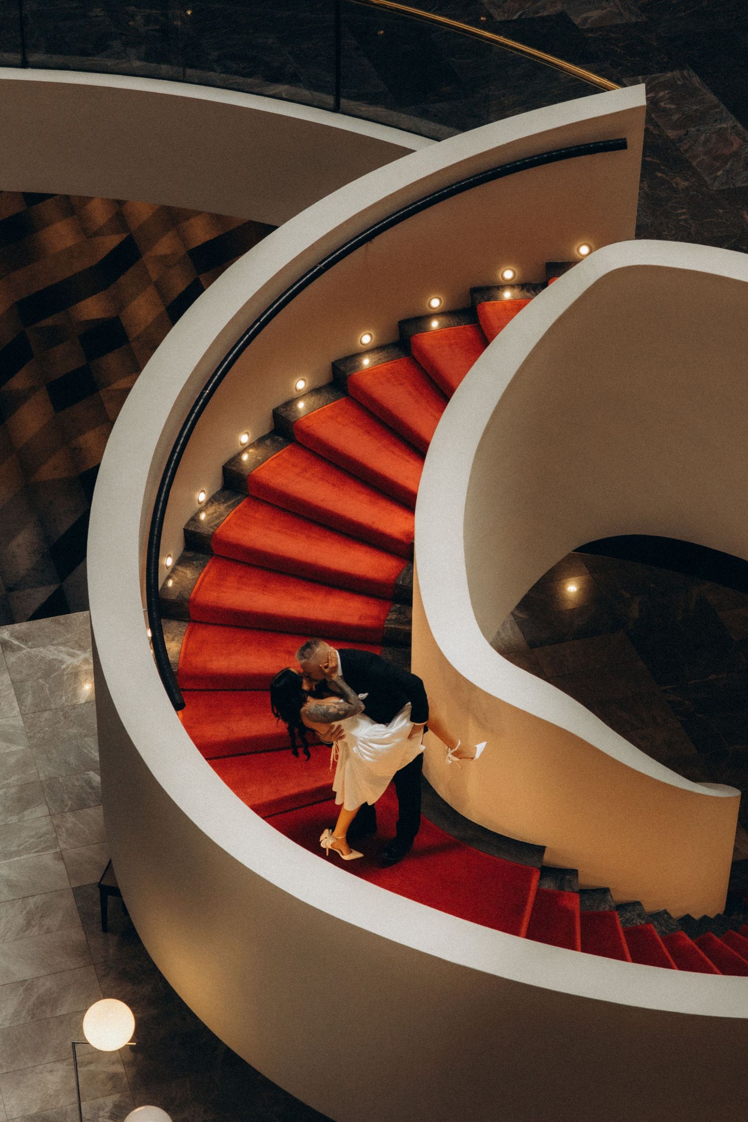 Spiral staircase with red carpet and dramatic lighting creating elegant curves.