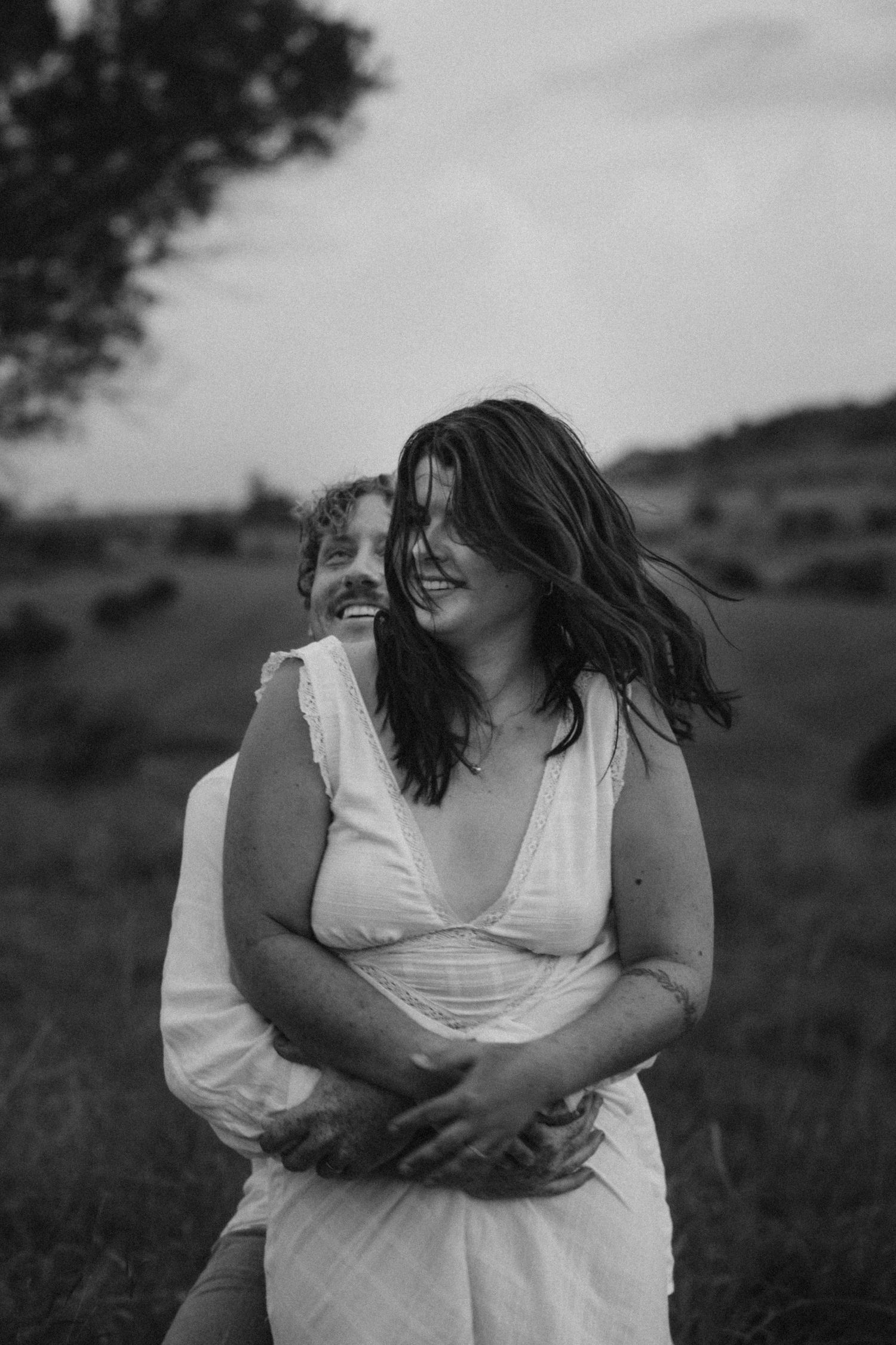 Intimate black and white portrait of a couple embracing in a field.