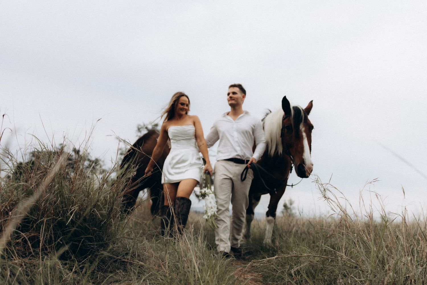 Panoramic view of a wedding couple walking with their horse through tall grass.