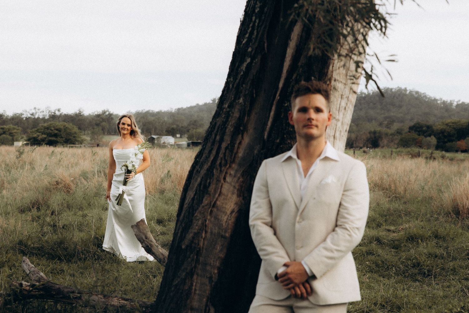 Wedding couple poses near a tree in a rustic outdoor setting.