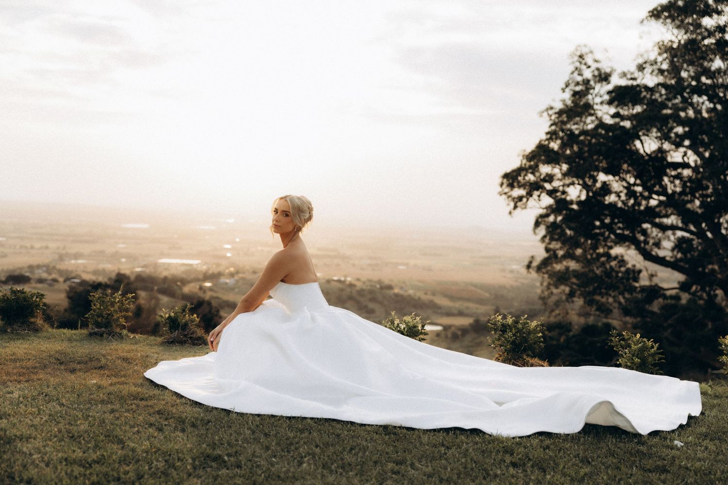 White wedding dress train flows elegantly across a hilltop during golden hour.