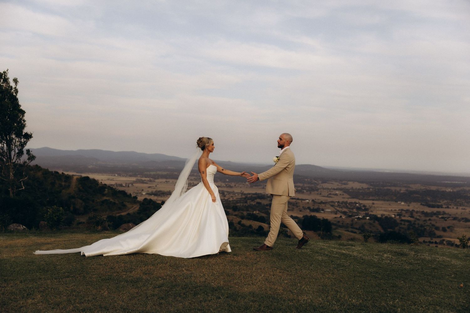 Scenic panoramic view of a wedding couple walking on a hilltop against a cloudy sky.