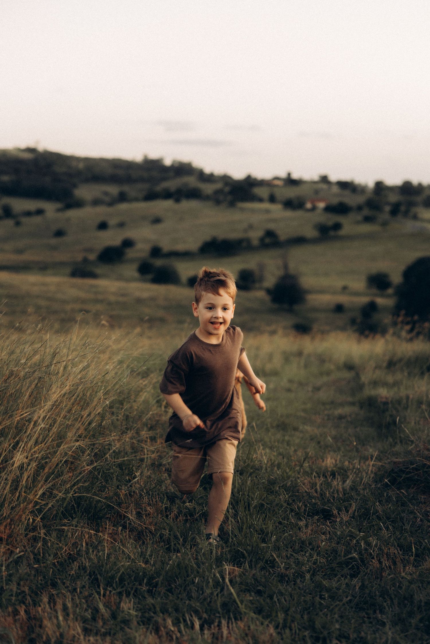 A child plays energetically in a grassy field with rolling hills in the background.