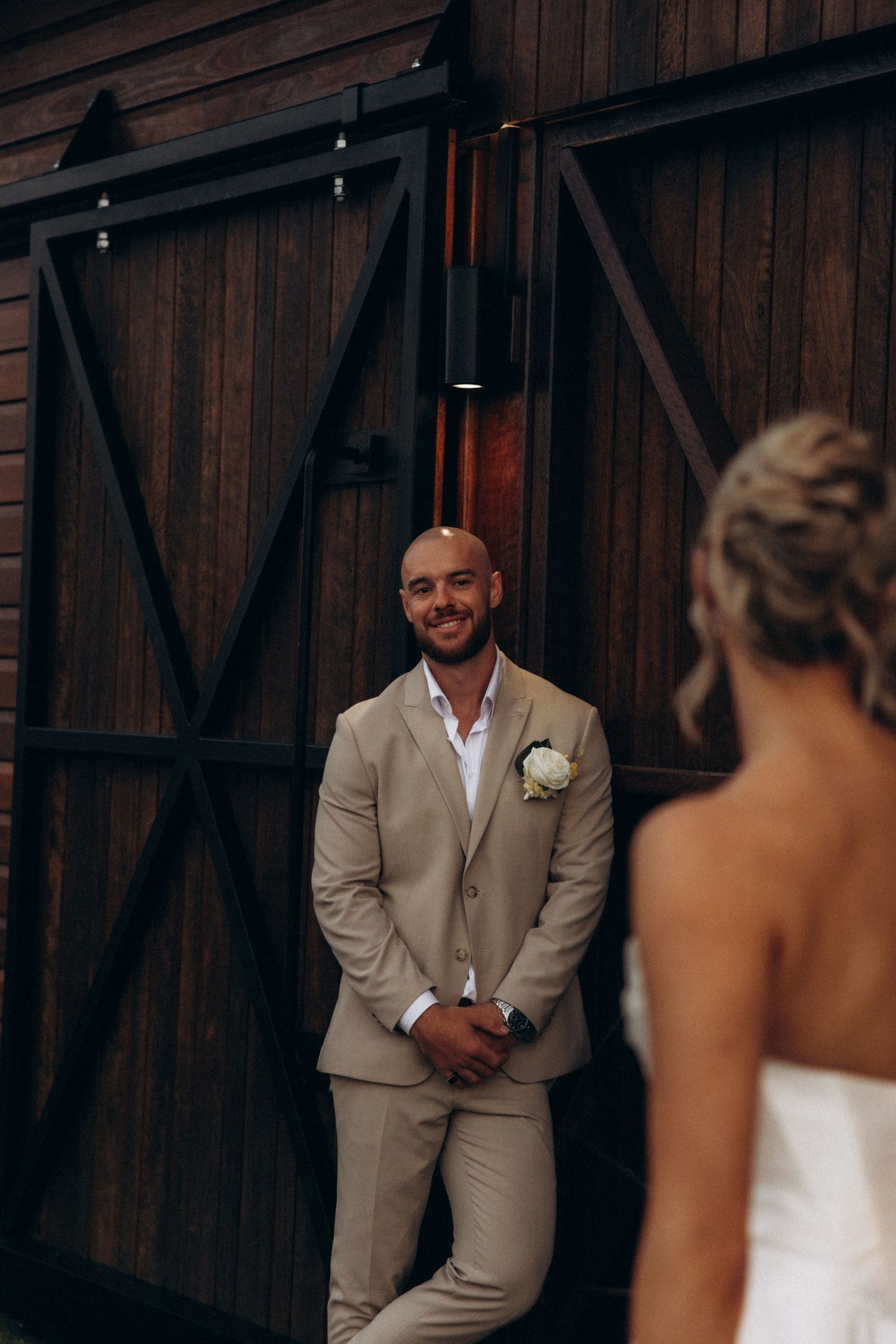 Wedding couple shares a playful first look moment outside a wooden barn.