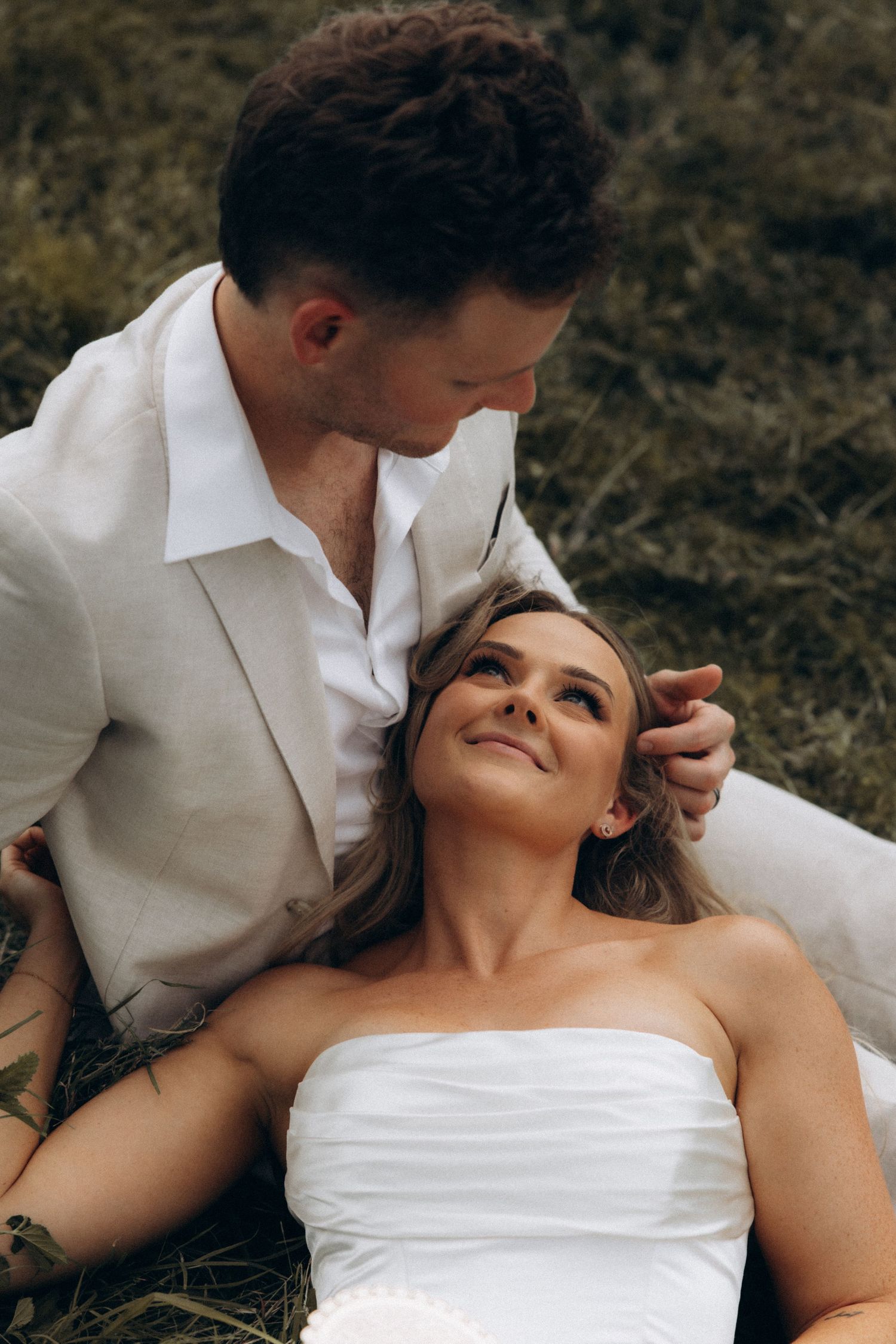 A couple in white clothing shares tender moments while reclining on the ground.