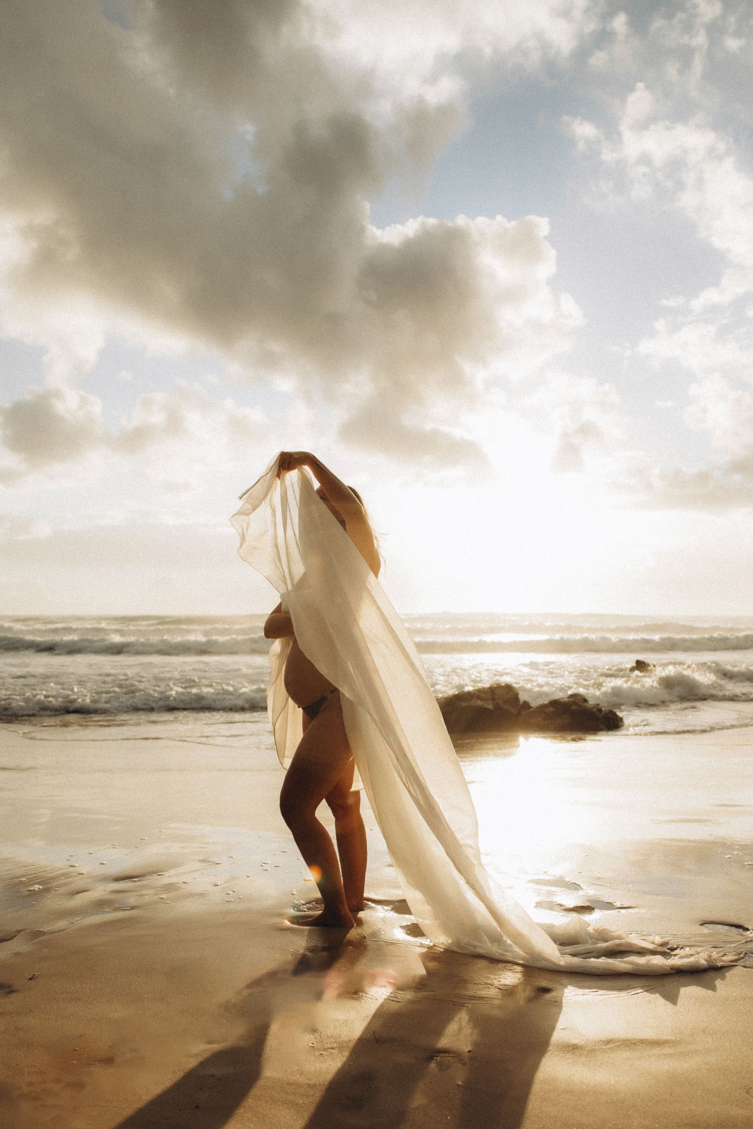 Flowing white fabric catches the wind on a dramatic beach at golden hour.