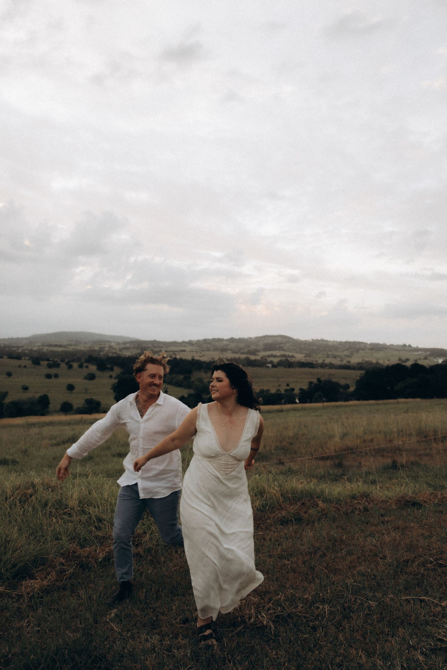 Couple playfully running and dancing together in a scenic field at dusk.