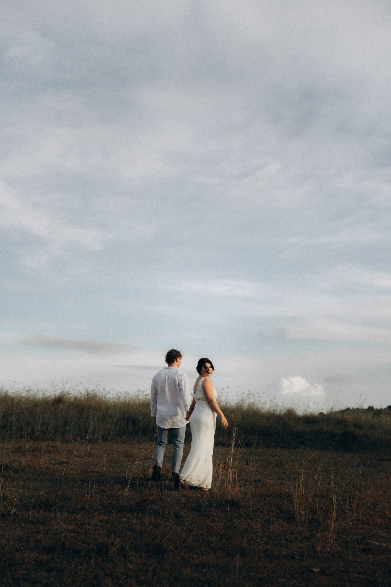 A couple walks together on a hilltop against a moody sky.