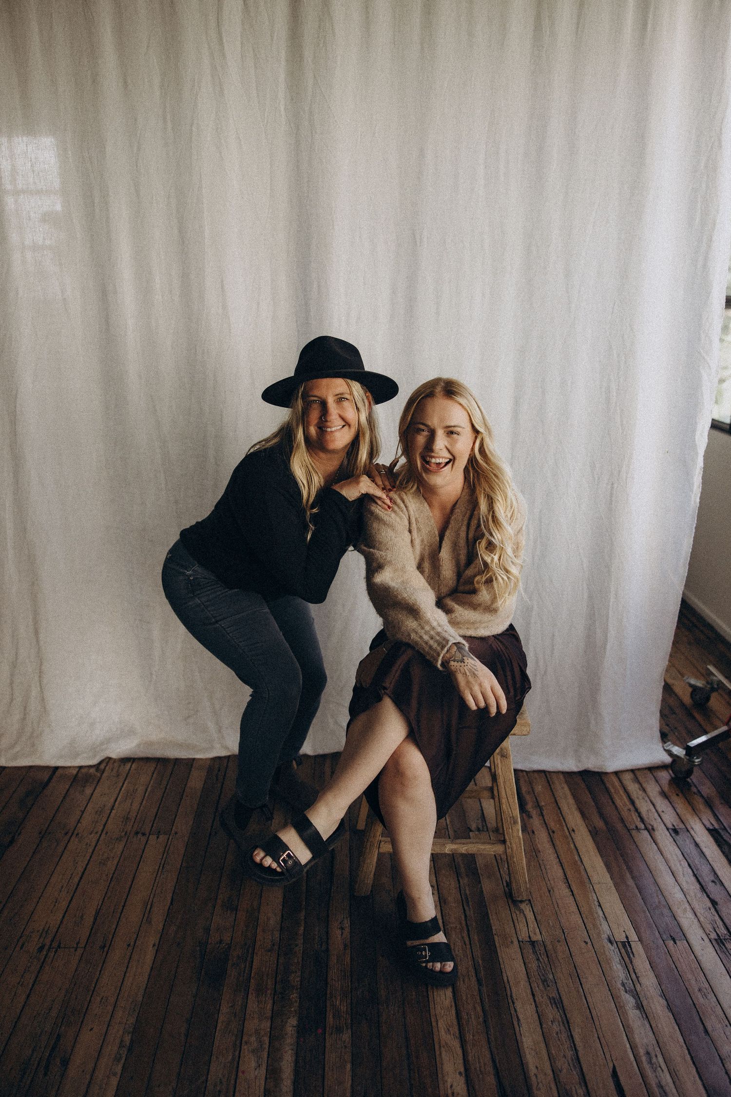 Studio photoshoot on wooden floor showing friends in casual attire having fun together.