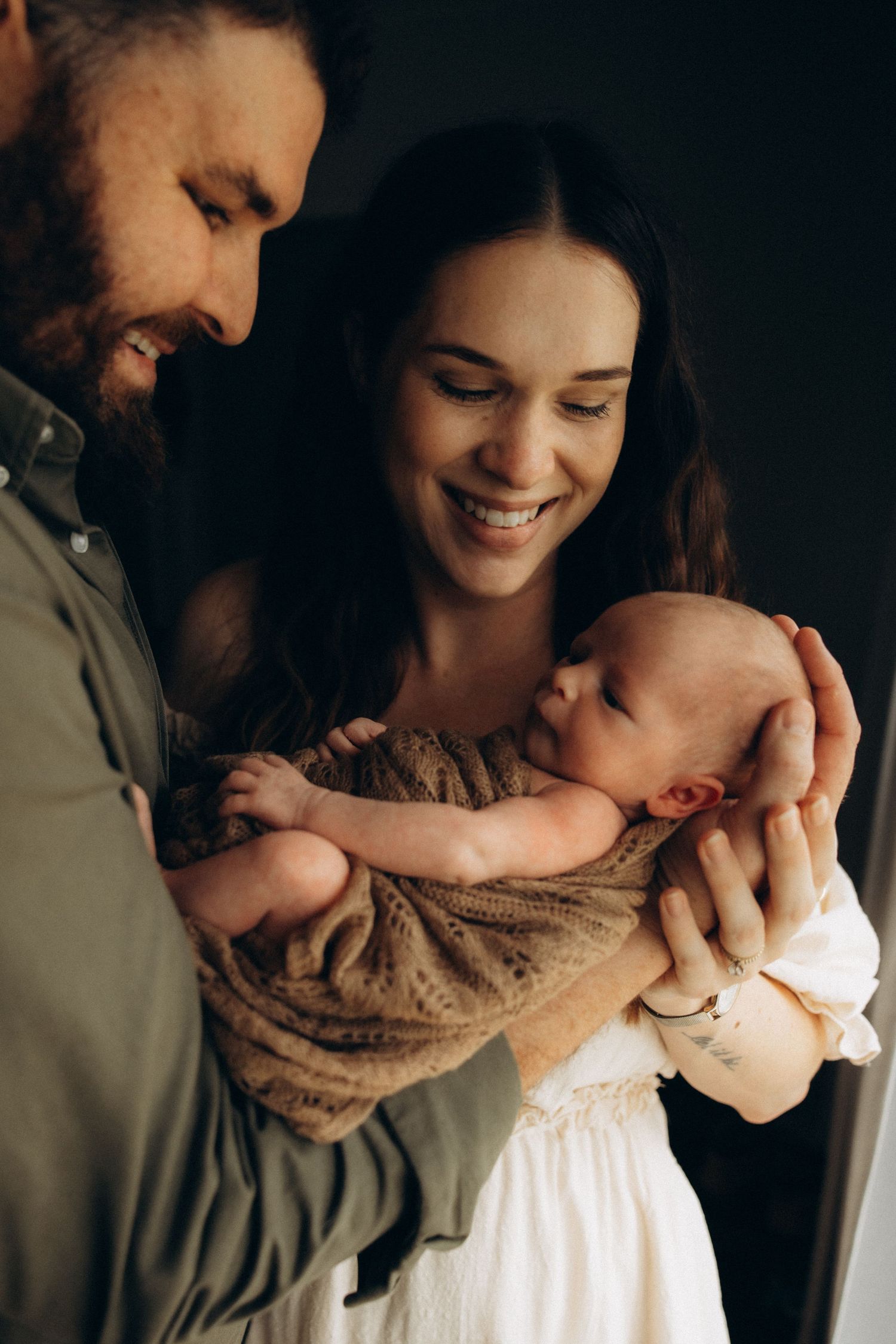 Intimate family moment with newborn baby wrapped in brown blanket.